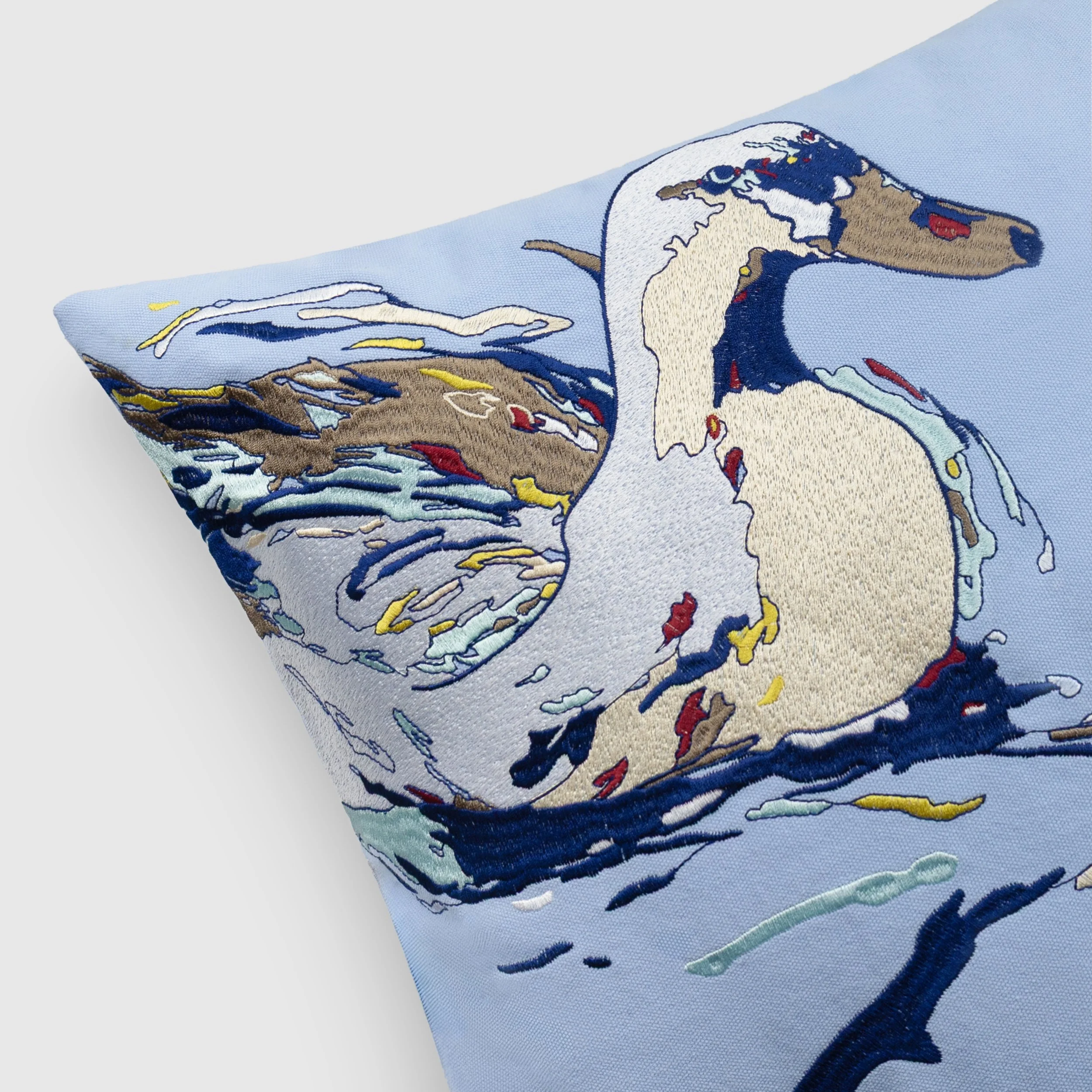 Close-up of Drift embroidered throw pillow showing detailed embroidery of a duck, with layered stitching, flowing water motifs, and intricate color variations.