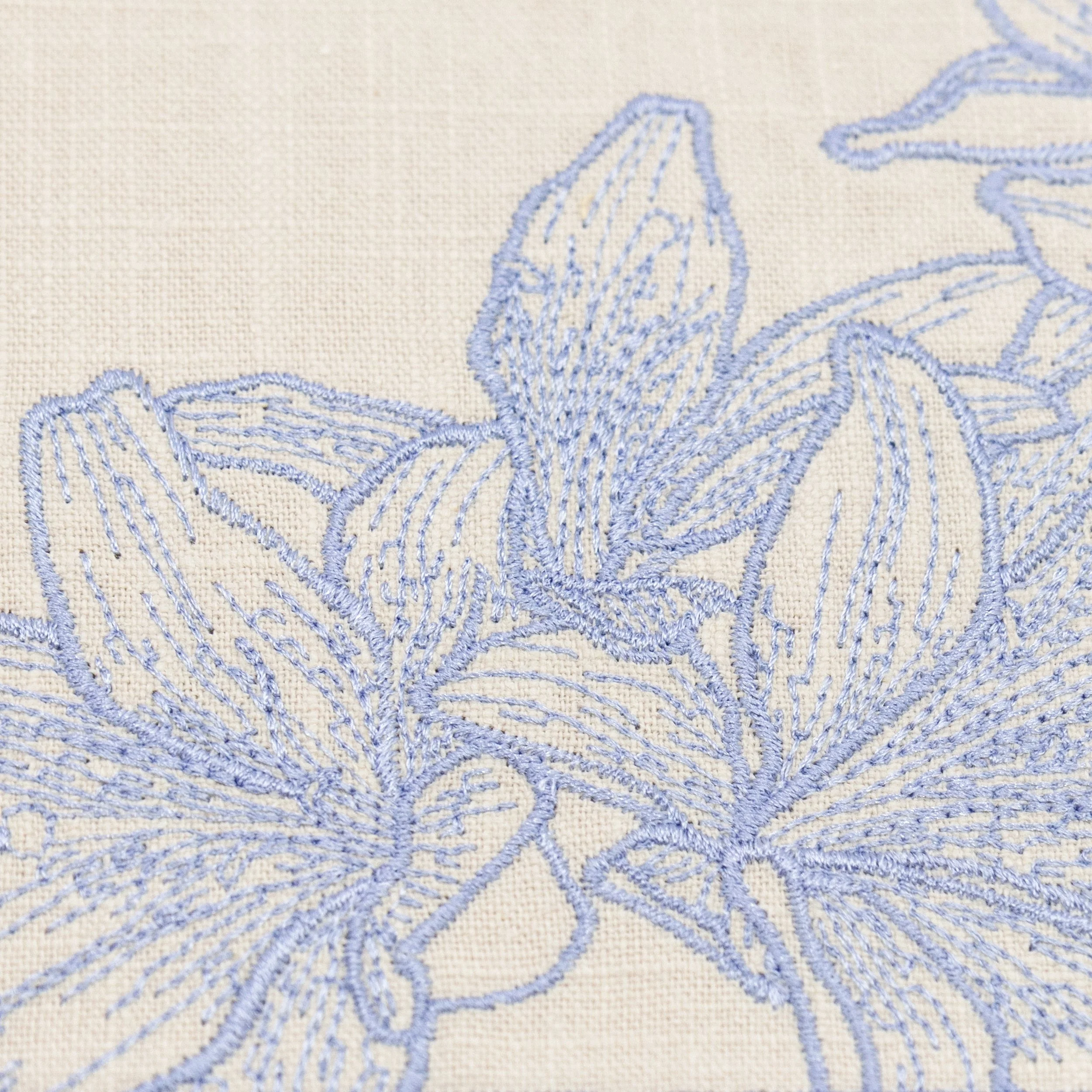 Close-up embroidery detail of blue lily flowers stitched on a natural linen-look placemat