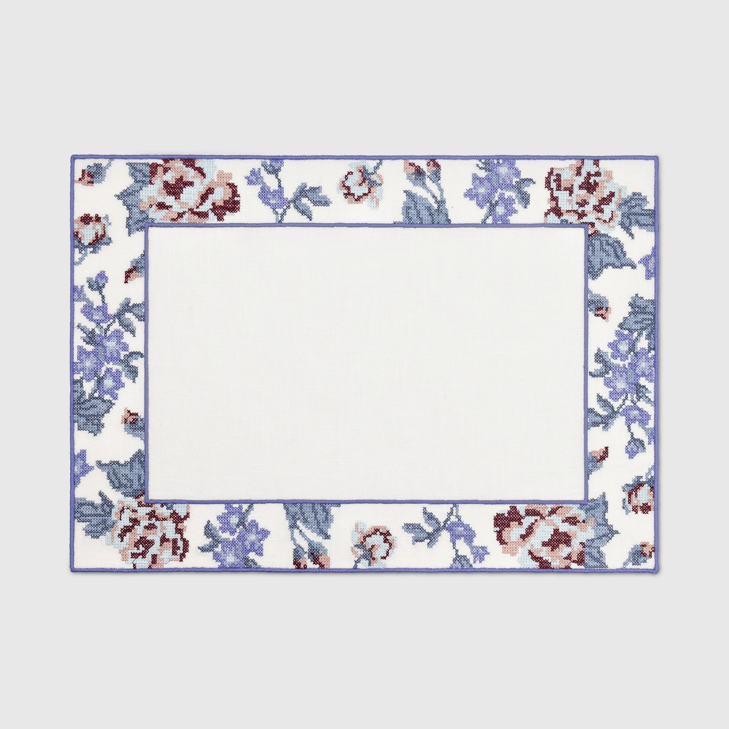Cross-stitch floral embroidered placemat with lavender, blue, blush, and burgundy flowers on a white background