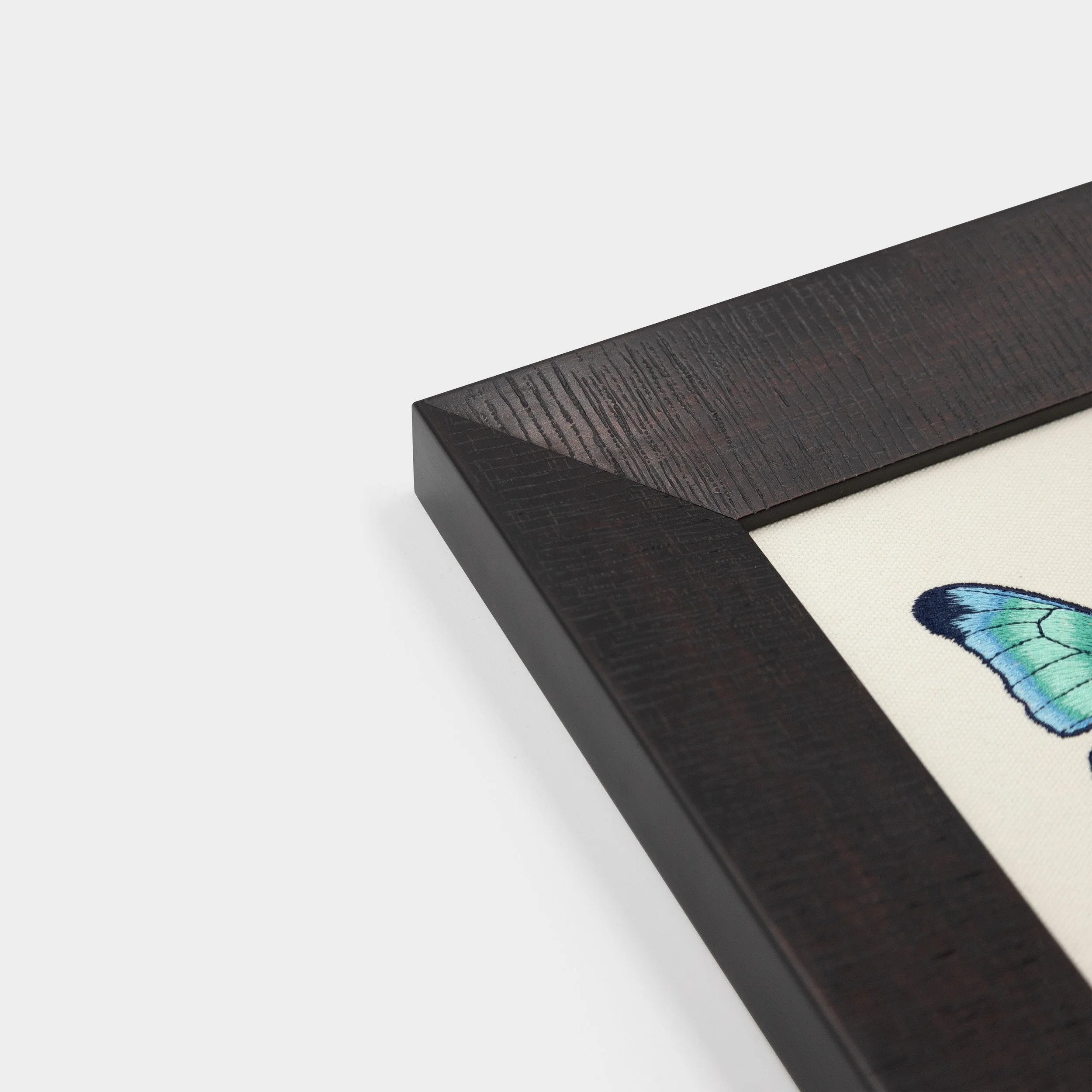 Corner detail of the substantial dark solid wood frame surrounding the Aetheria butterfly embroidered artwork.
