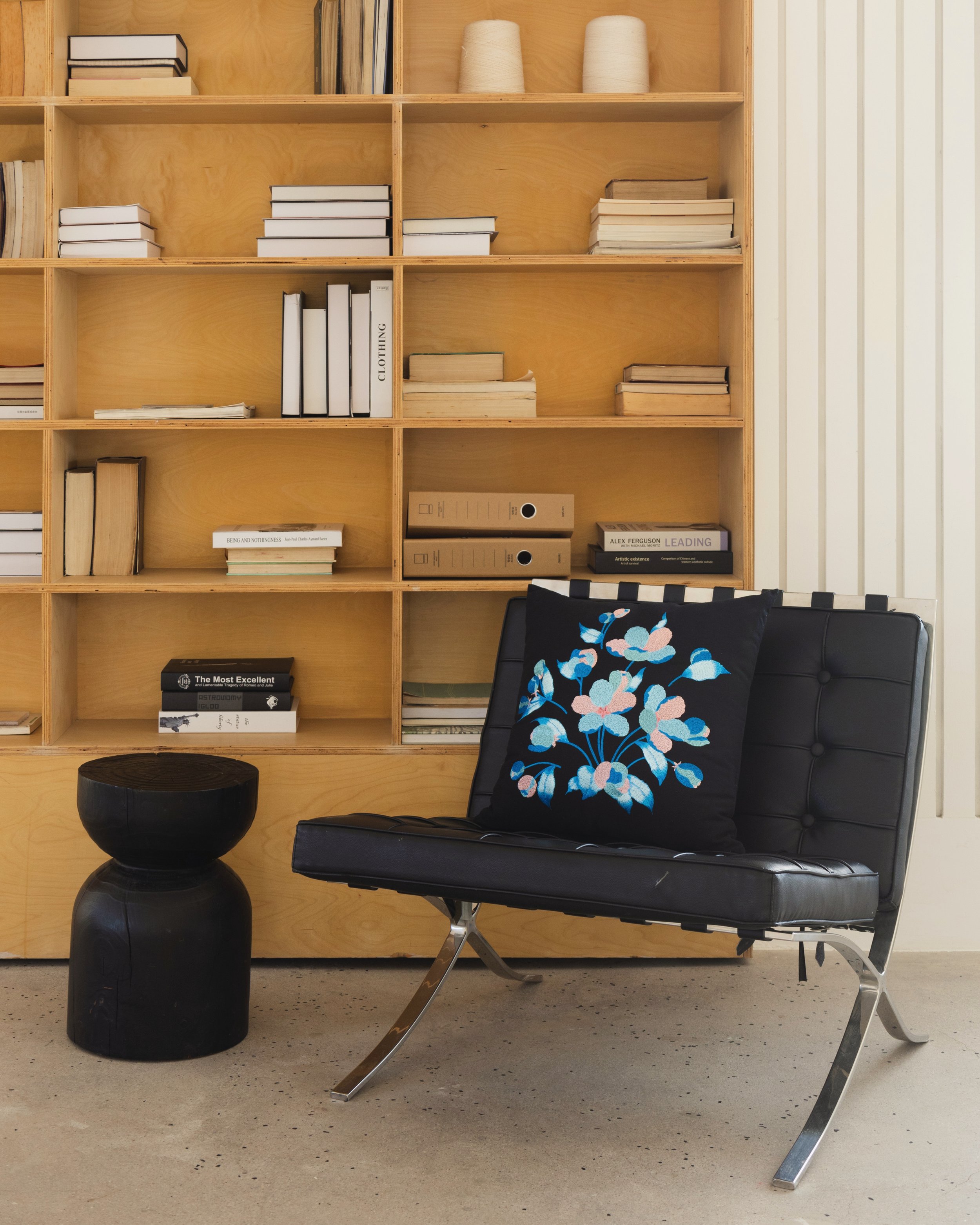 Embroidered throw pillow from the Etherelle series on a black leather chair in front of a bookshelf.jpg
