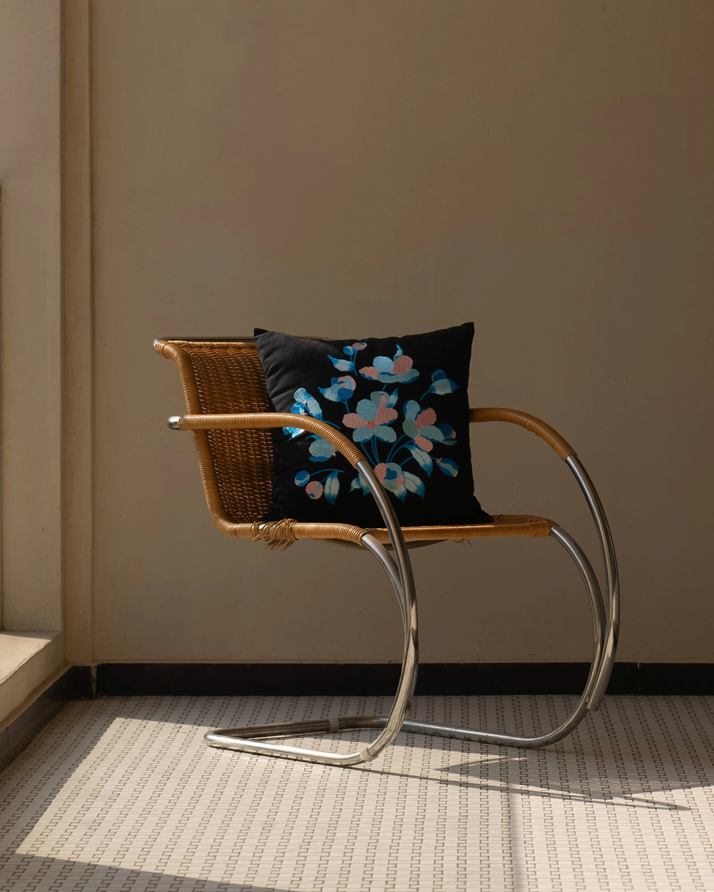 Embroidered throw pillow from the Etherelle series placed on a modern metal chair.jpg
