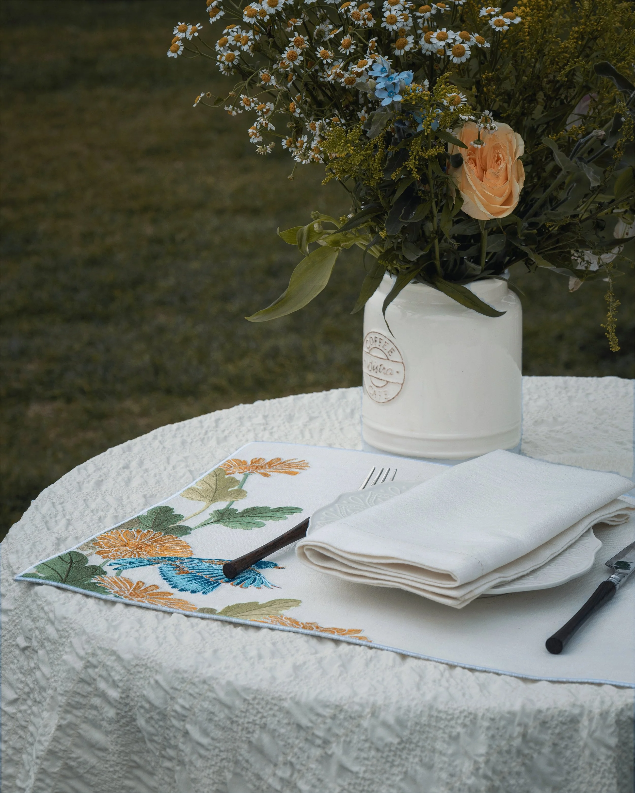 Nature-inspired botanical embroidered placemat and hemstitched napkin on a outdoor dining table.jpg