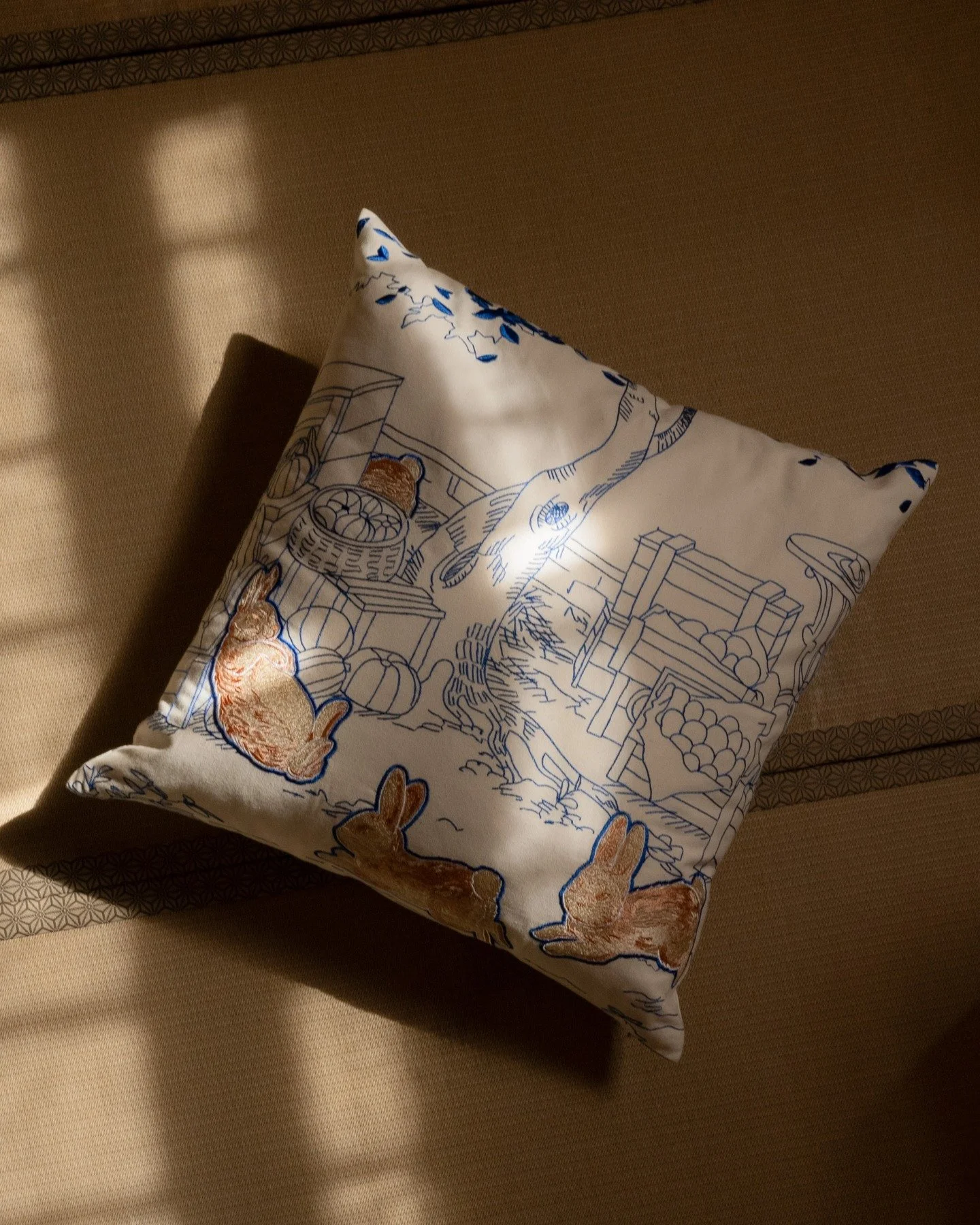 Whimsy Throw Pillow.

Fully embroidered on soft cotton, with light catching the texture and bringing out each detail &mdash; from the small bunny figures to the toile-inspired linework in the background.

An easy piece for a chair, a sofa, or a quiet