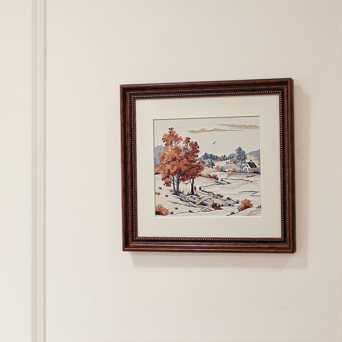 Embroidered autumn landscape wall art hanging on a white wall