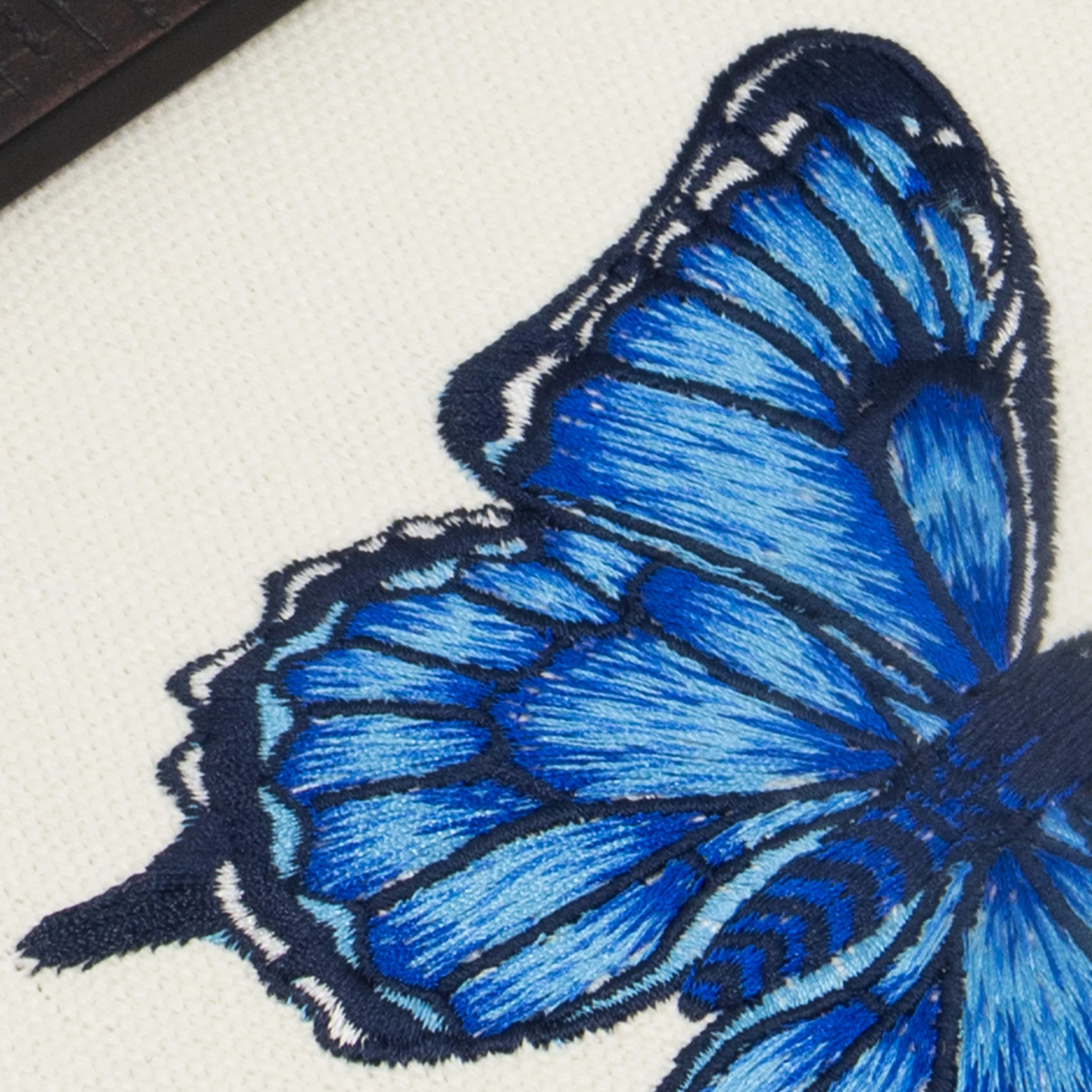 Close-up embroidery detail of the Nocturna butterfly showing fine-line stitching and blue tonal gradients across the wings