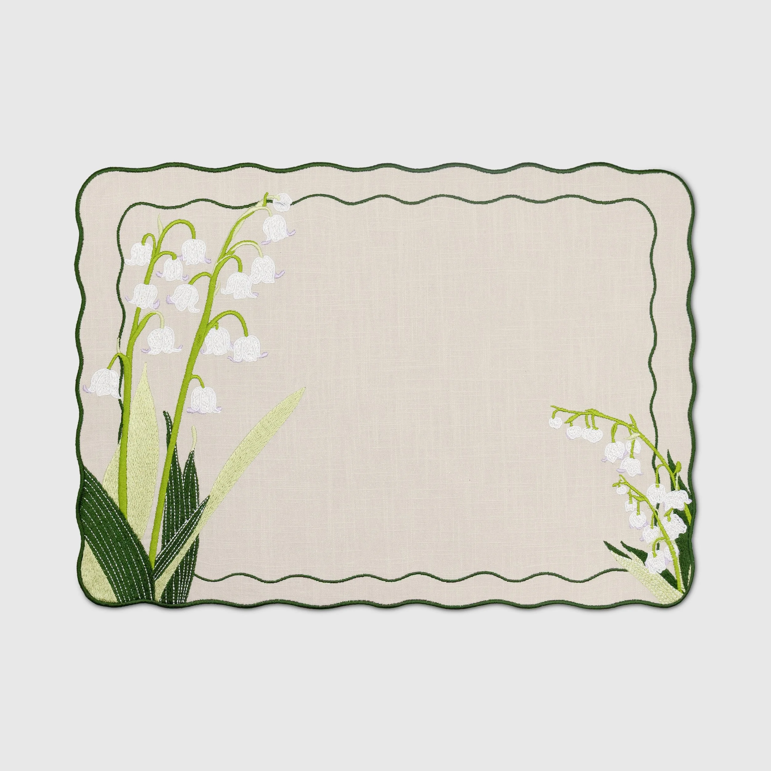 Lily of the valley embroidered placemat with scalloped green border on a natural linen-blend fabric