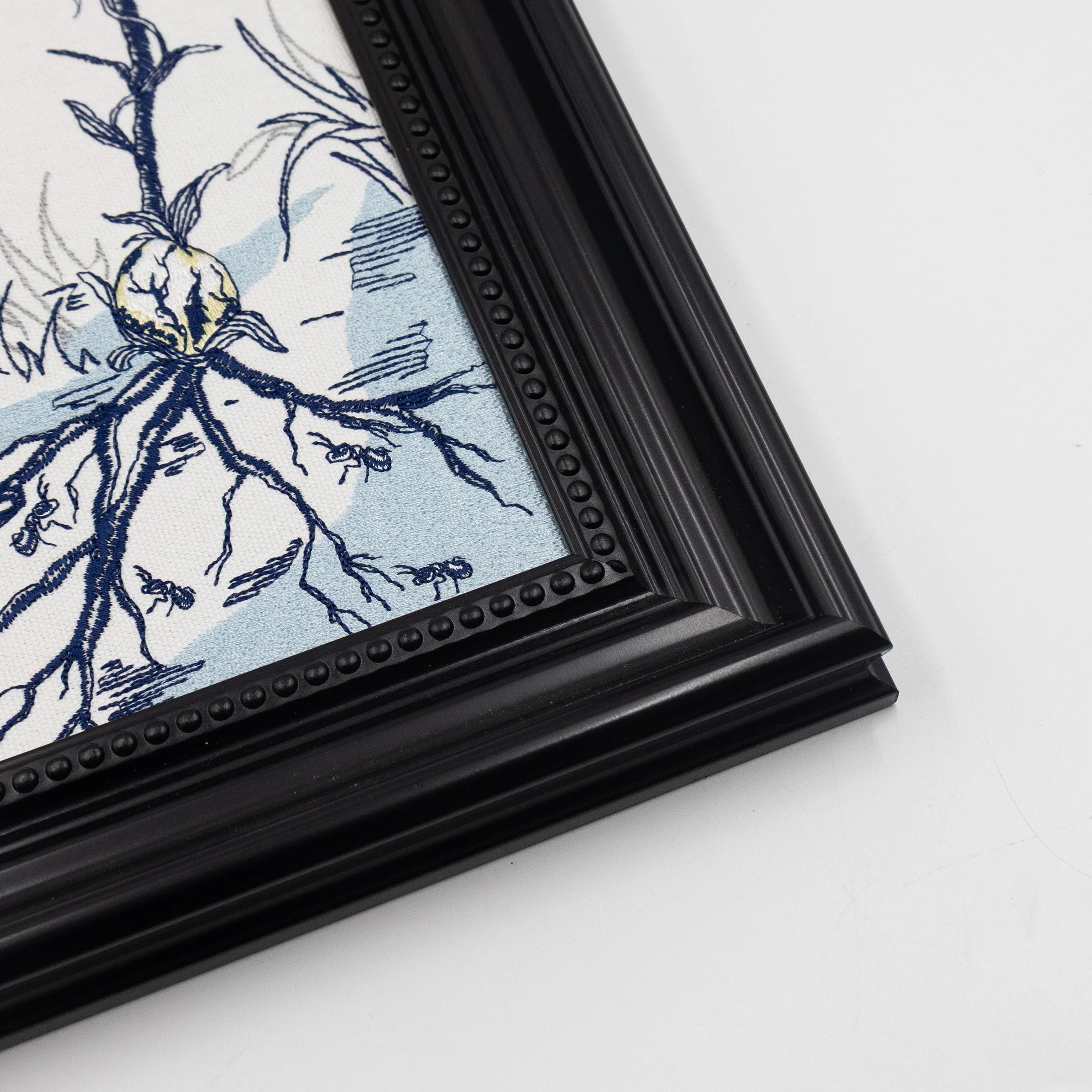 Close-up of the black decorative frame and embroidered botanical details of the Sylvan framed wall art.