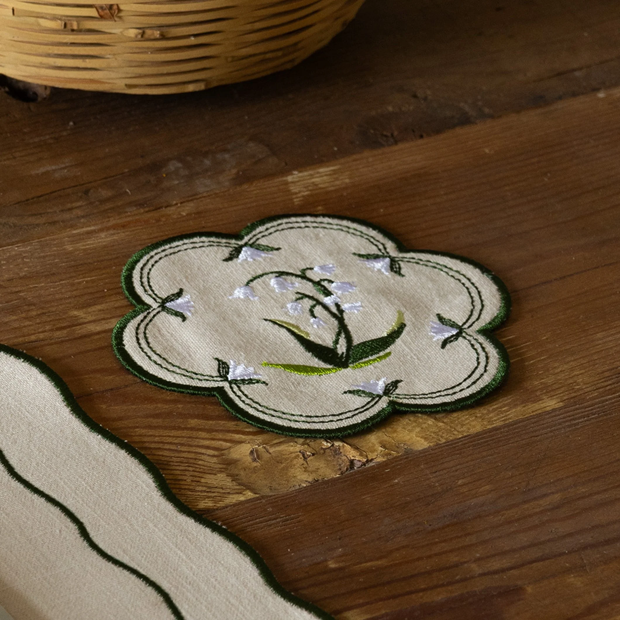 Lily of the valley embroidered coaster styled on a rustic wooden table beside a matching placemat