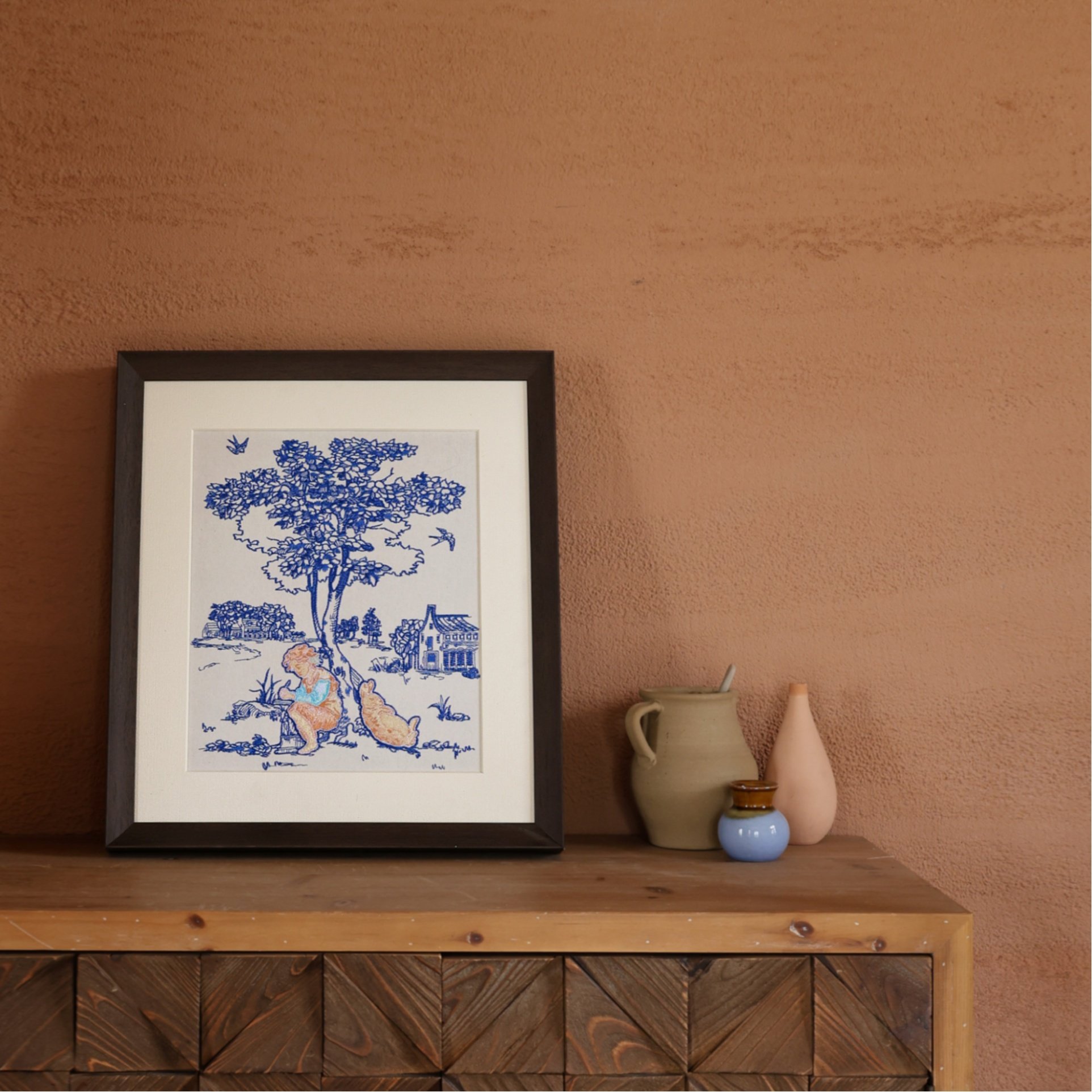 Embroidered framed art of a child and a rabbit under the tree in front of a terracotta wall