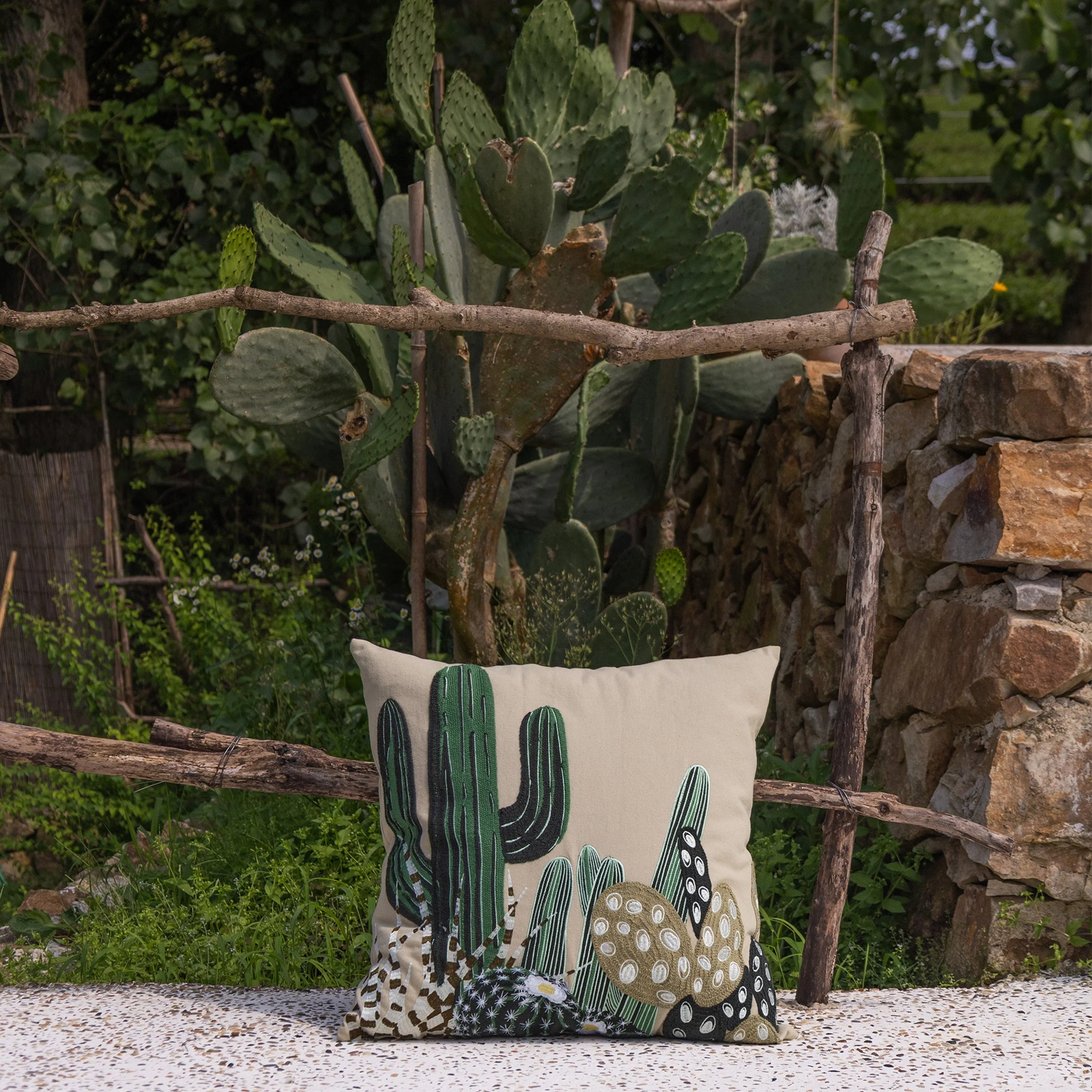Arid embroidered throw pillow featuring desert botanical embroidery displayed in a garden setting