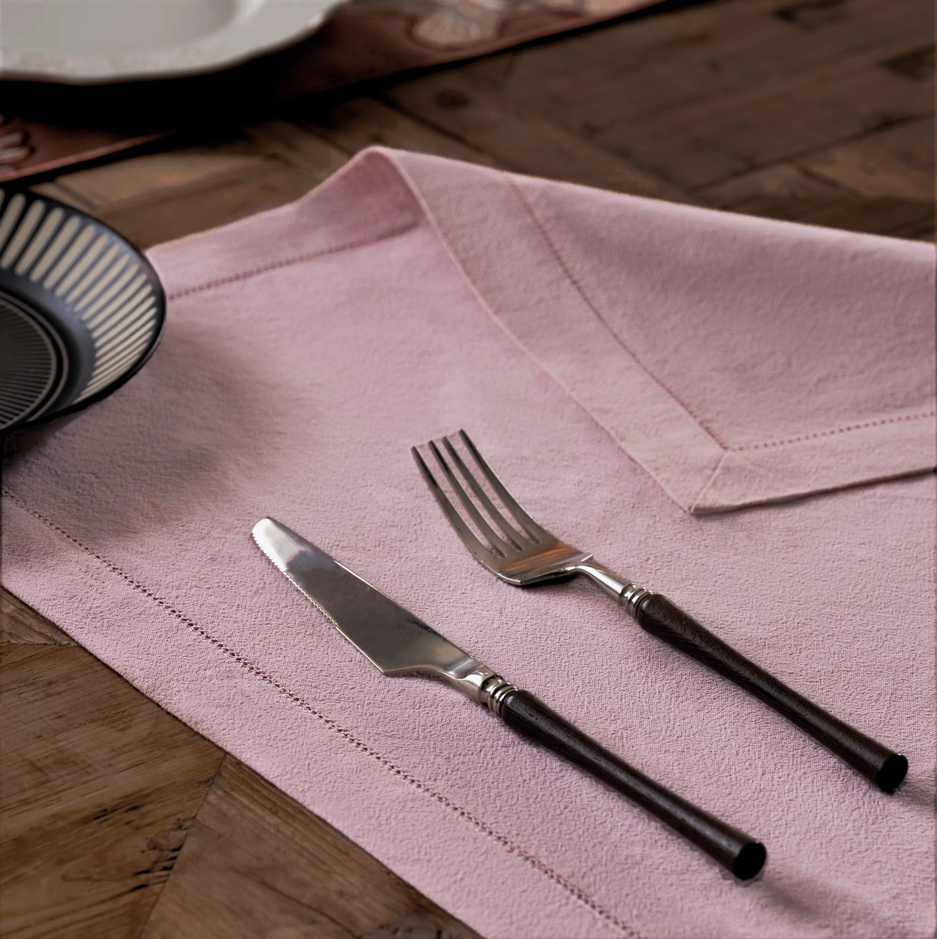 Pink cotton napkin with hemstitch embroidery details spread on a wooden table