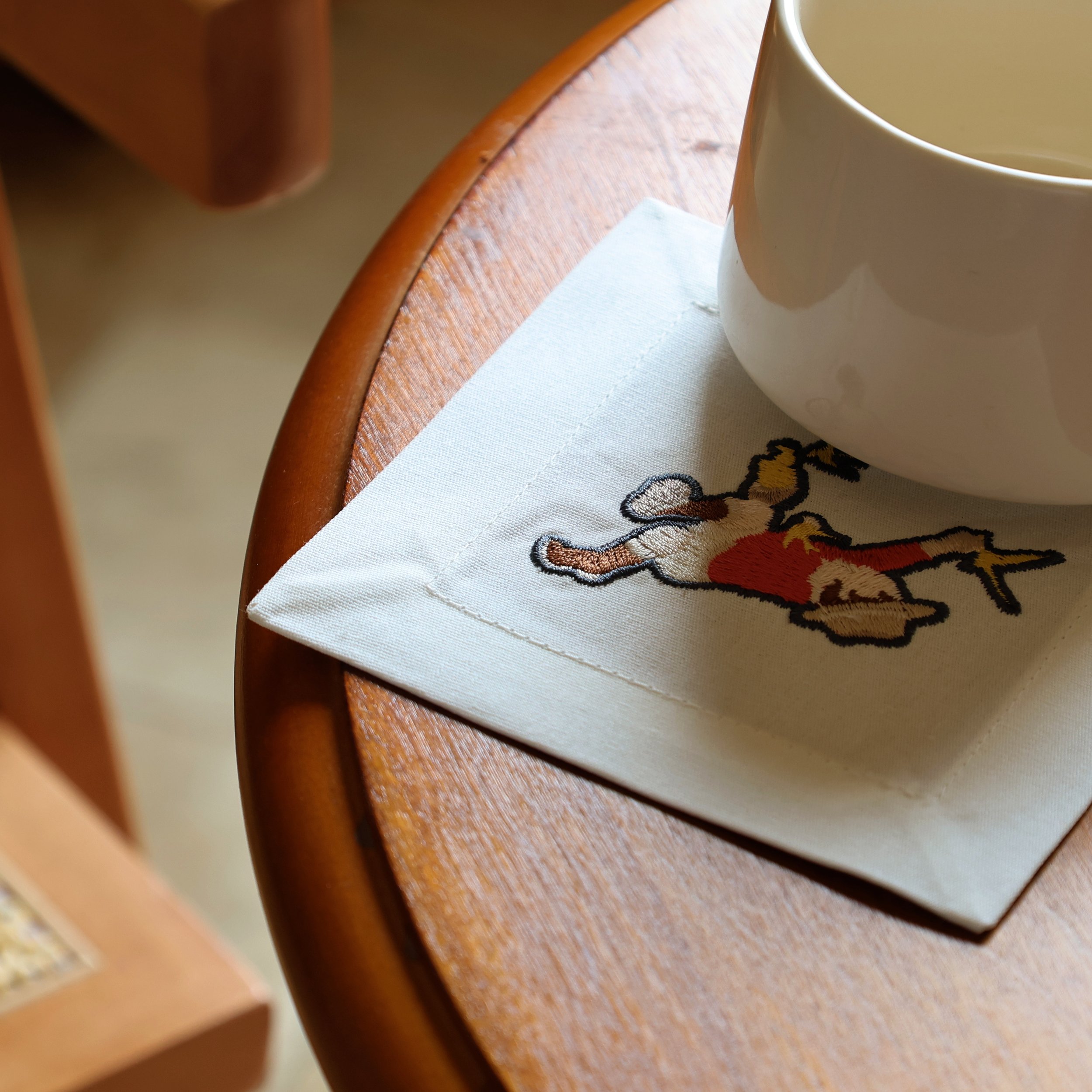 "Wild Corner" Cocktail Napkin on a Wooden Round Table With a Coffee Mug