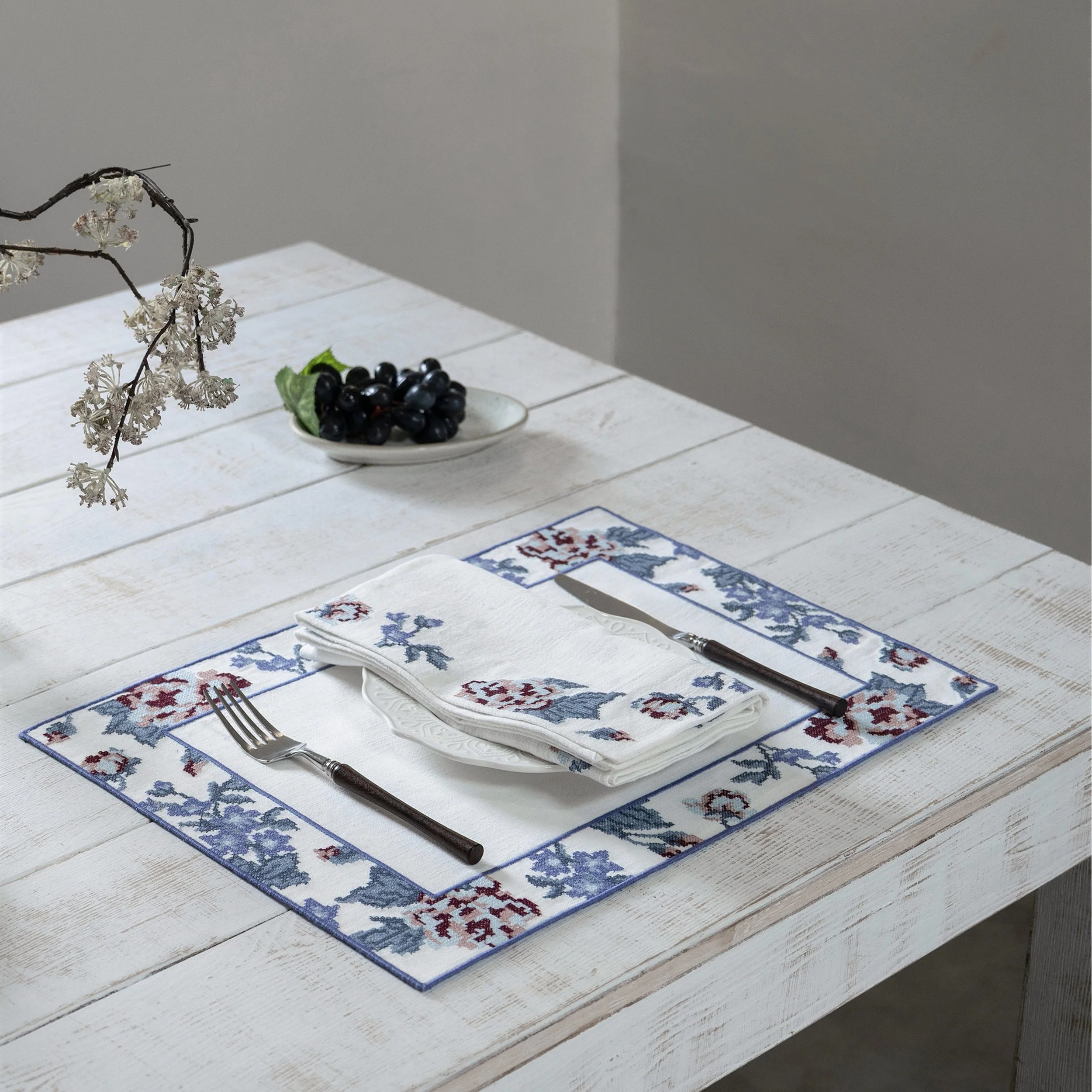 Bouquet cross-stitch embroidered placemat with matching napkin on a white wooden dining table