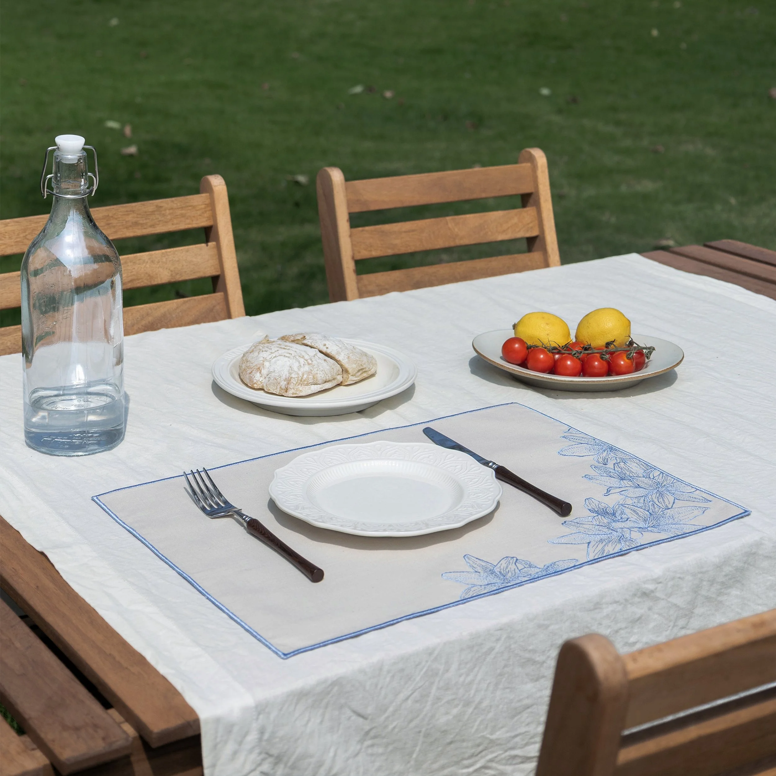 Lily embroidered placemat displayed on an outdoor dining table with white linen tablecloth and summer table setting
