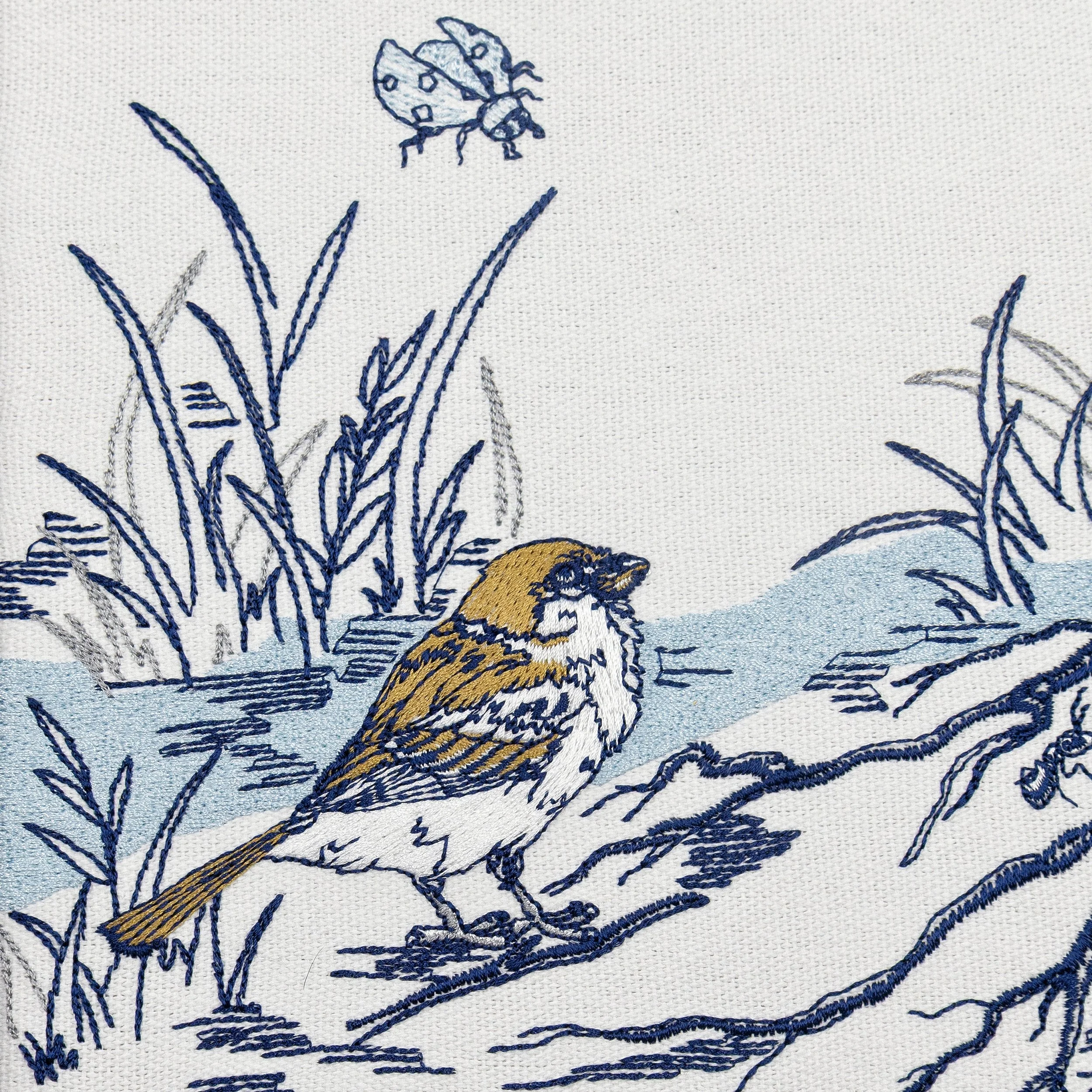 Close-up embroidery detail of a small bird and ladybug within the Sylvan botanical wall art, showing fine stitching and textured threadwork.
