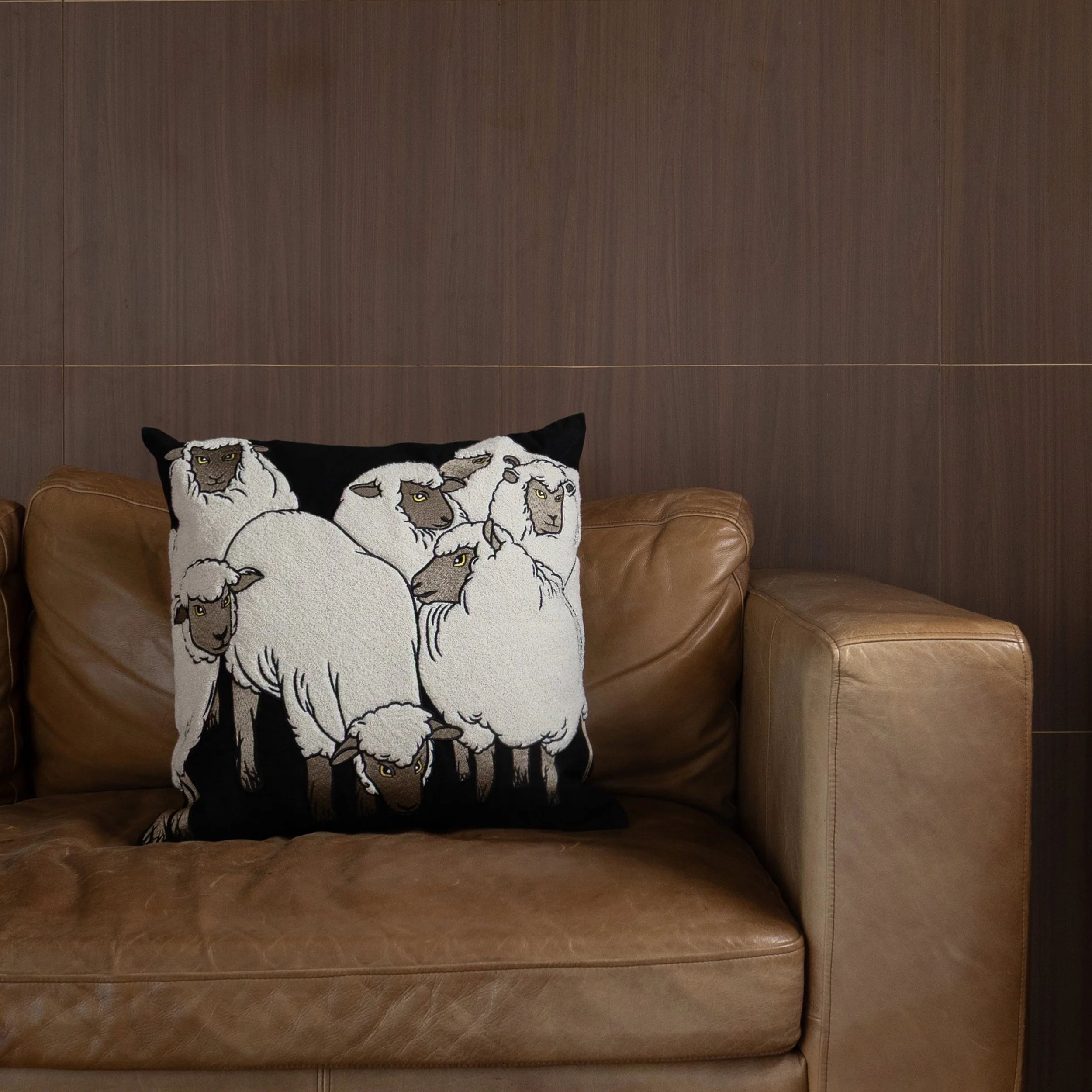 Sheep embroidered throw pillow on a brown leather sofa in a contemporary living room