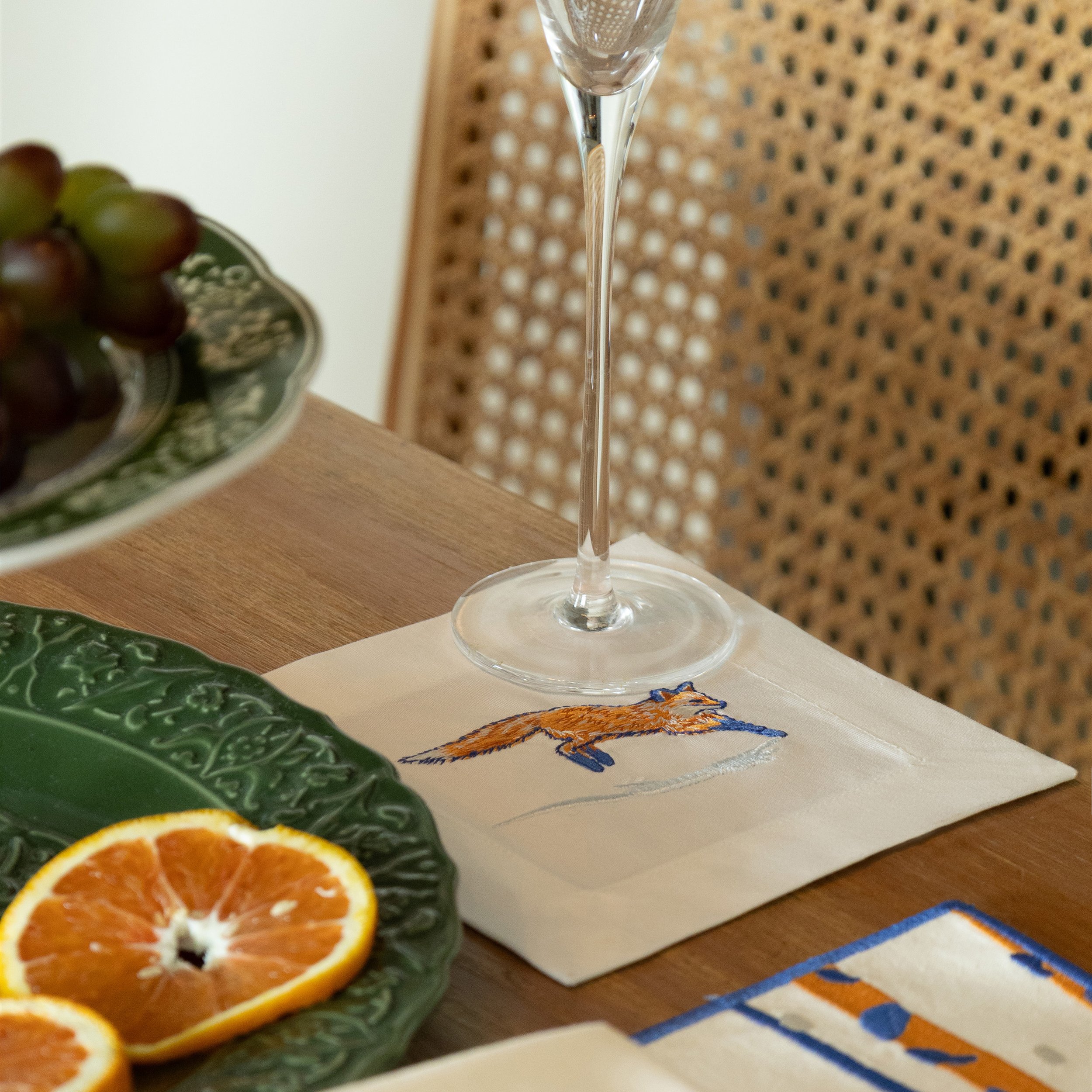 Fox cocktail napkin with embroidered fox design placed under a wine glass on a dining table