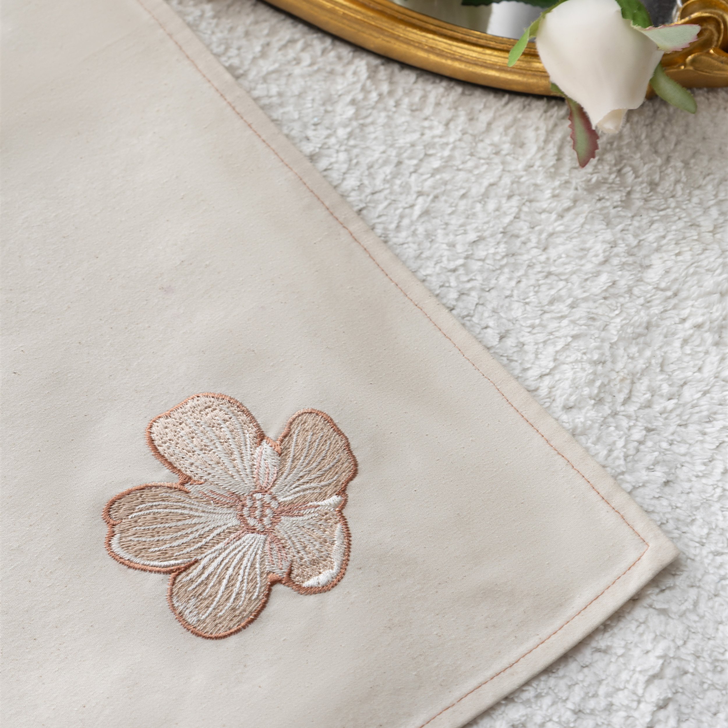 Close-up of the Dionaea Embroidered Napkin, featuring a soft beige fabric with a blush-toned floral embroidery near the corner.
