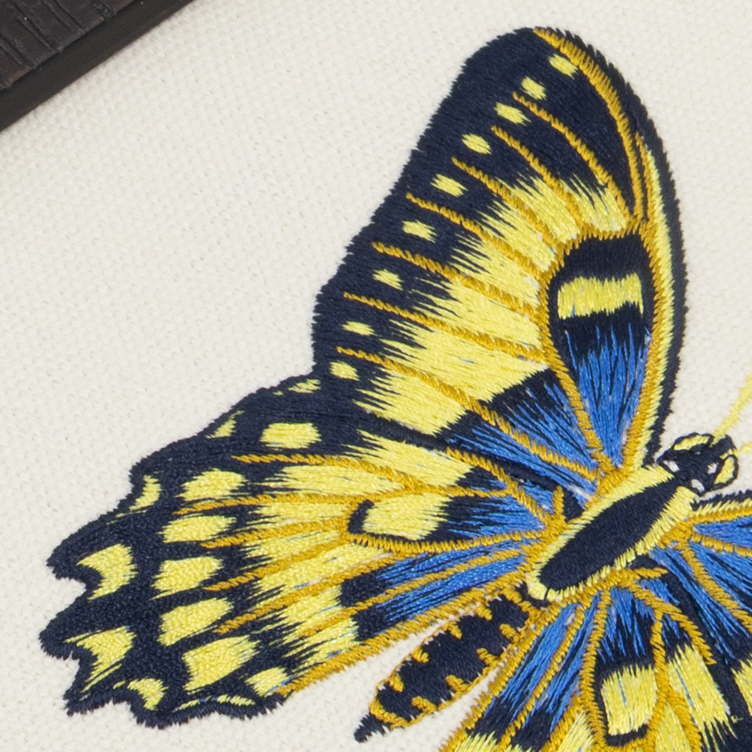 Close-up detail of Luminara butterfly embroidery showing intricate blue and yellow stitching on natural cotton fabric.