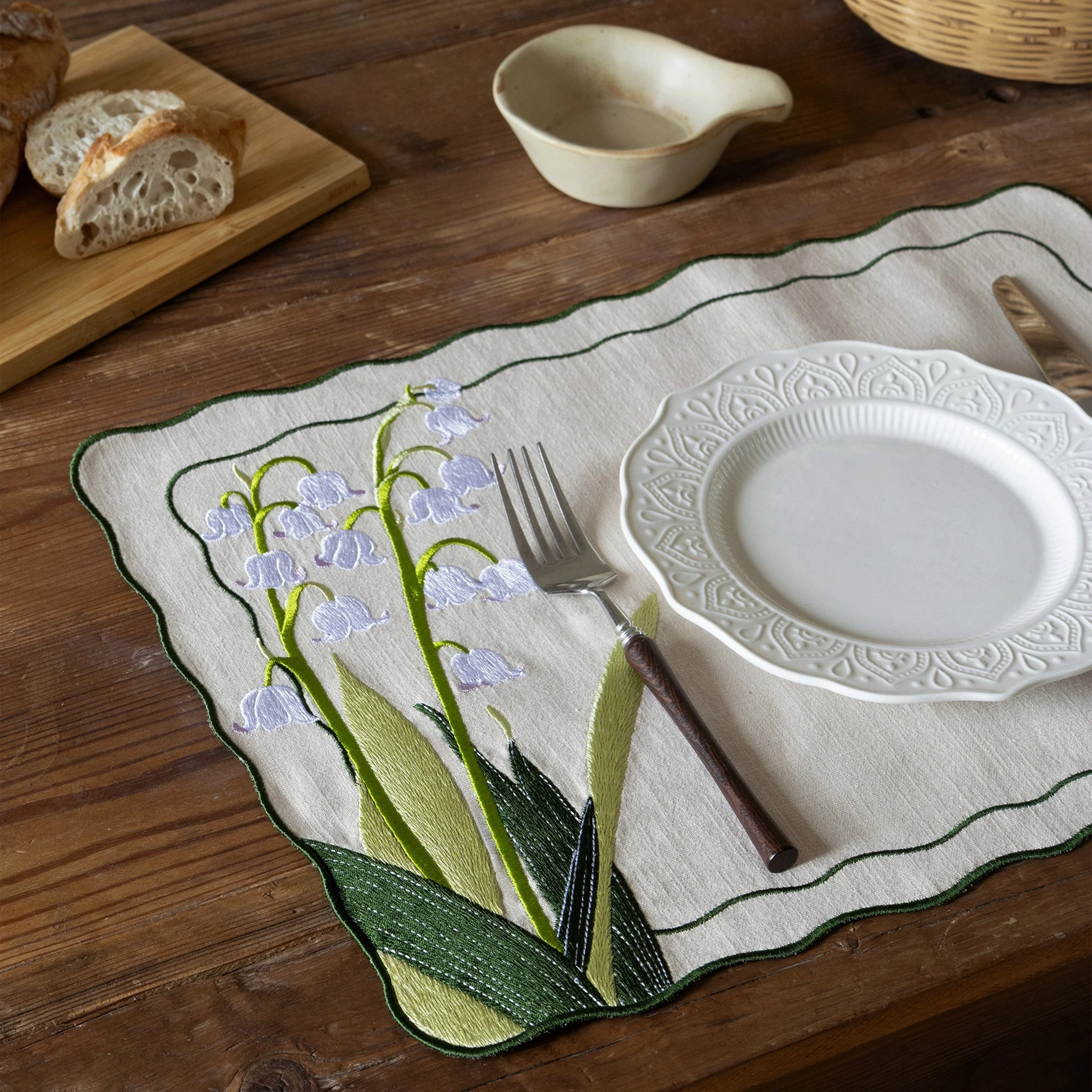 Botanical embroidered placemat featuring lily of the valley flowers styled on a wooden dining table