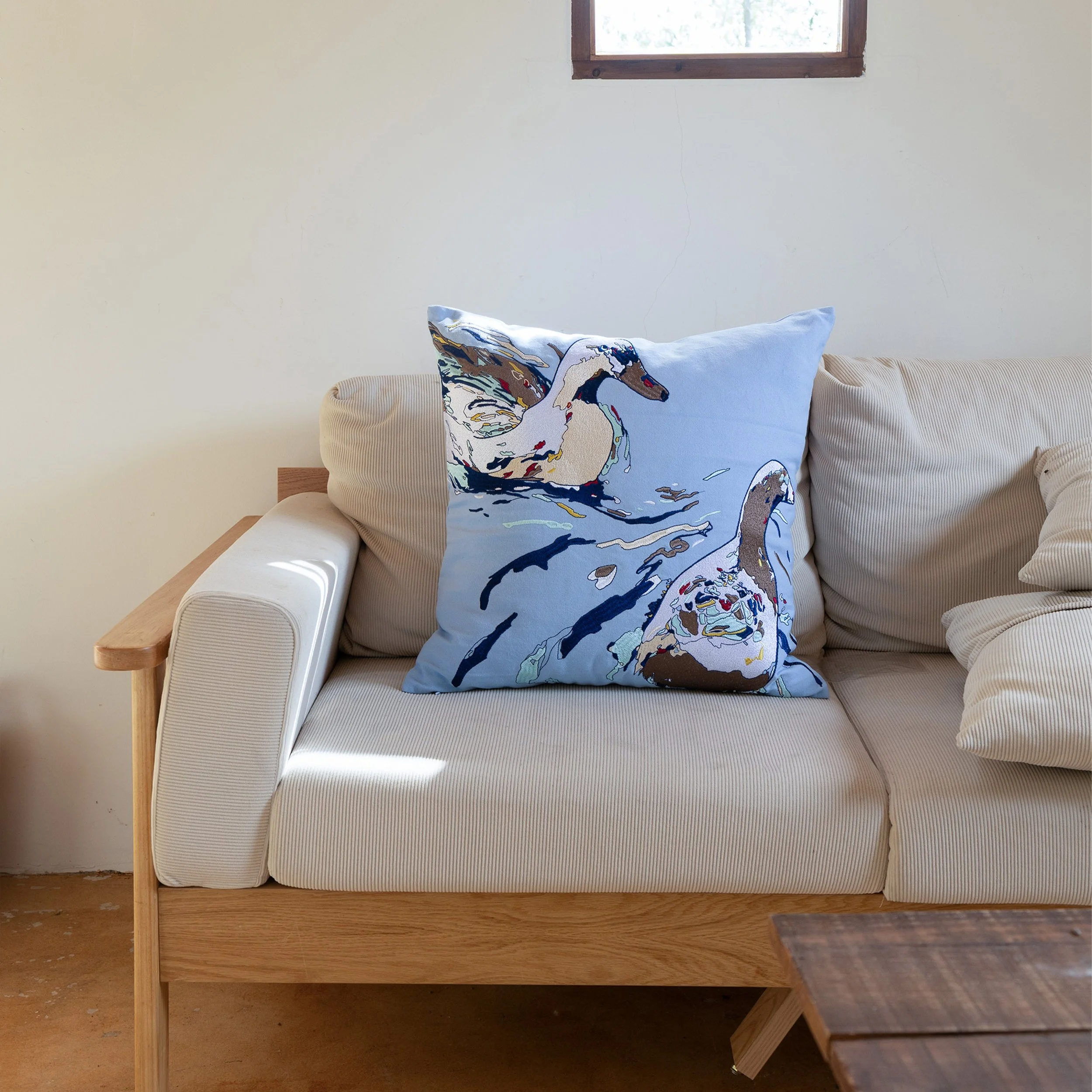 Drift embroidered throw pillow placed on a cream-colored sofa, bringing soft blue tones and nature-inspired embroidery into a modern living room.