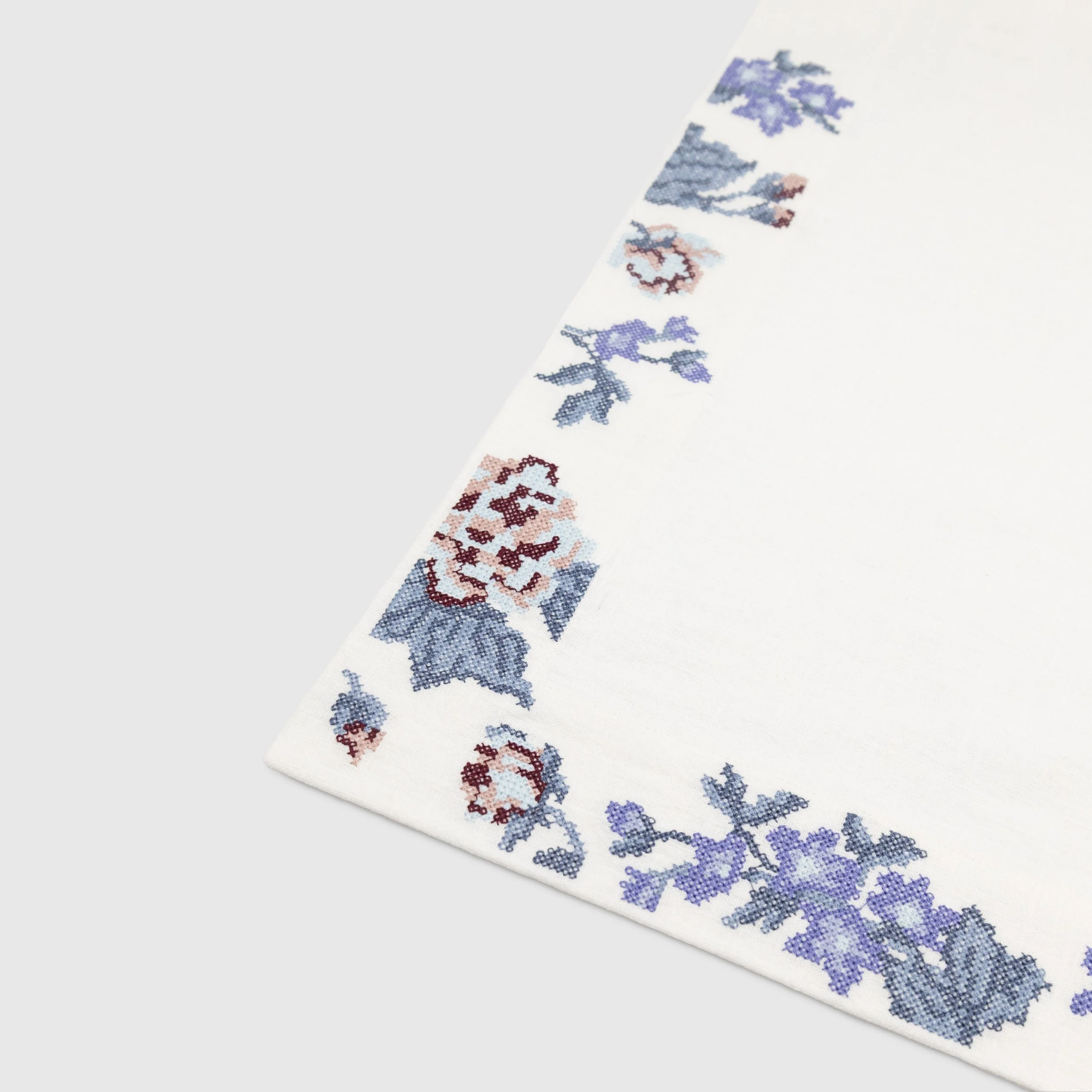 Close-up detail of Bouquet cross stitch floral embroidery showing blue and rose botanical motifs along the napkin border