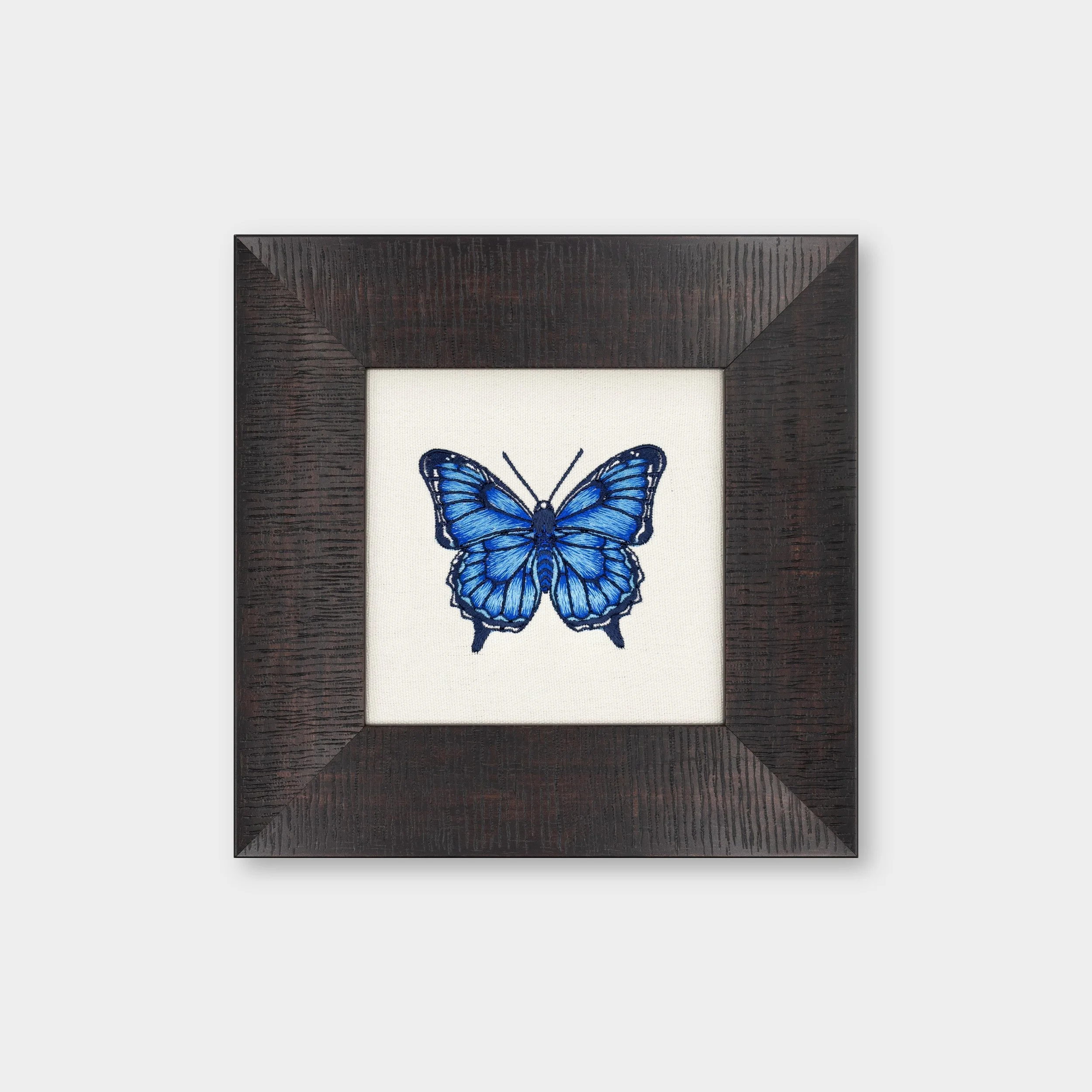 Nocturna butterfly embroidered wall art featuring a deep blue butterfly stitched on cotton fabric in a dark solid wood frame