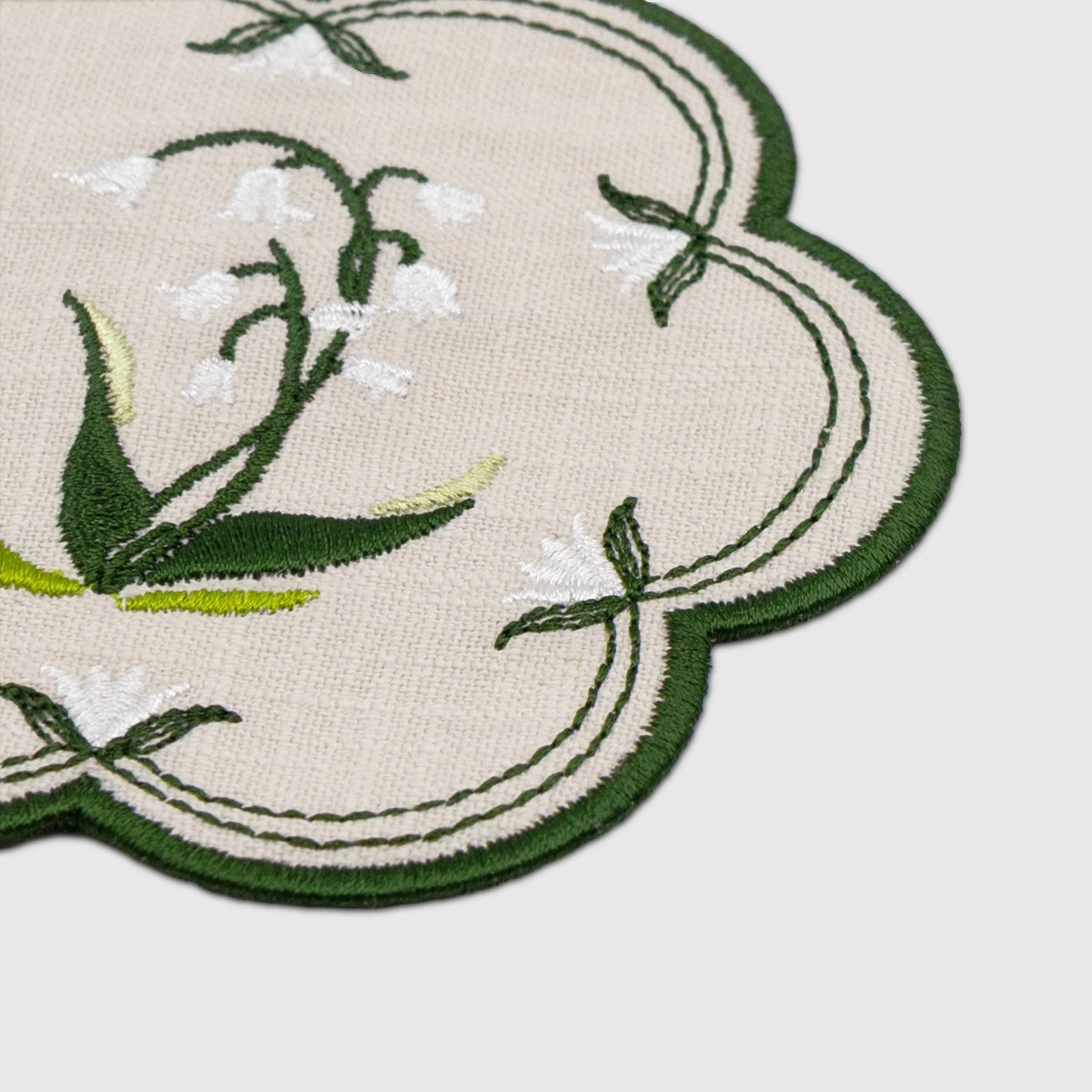 Close-up detail of lily of the valley embroidery and scalloped embroidered edge on a floral coaster