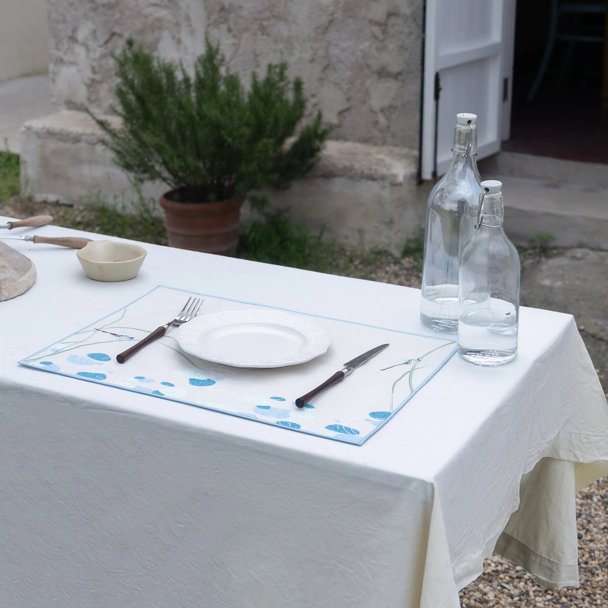 Dragonfly embroidered placemat displayed on an outdoor garden dining table with glass bottles and white table linen