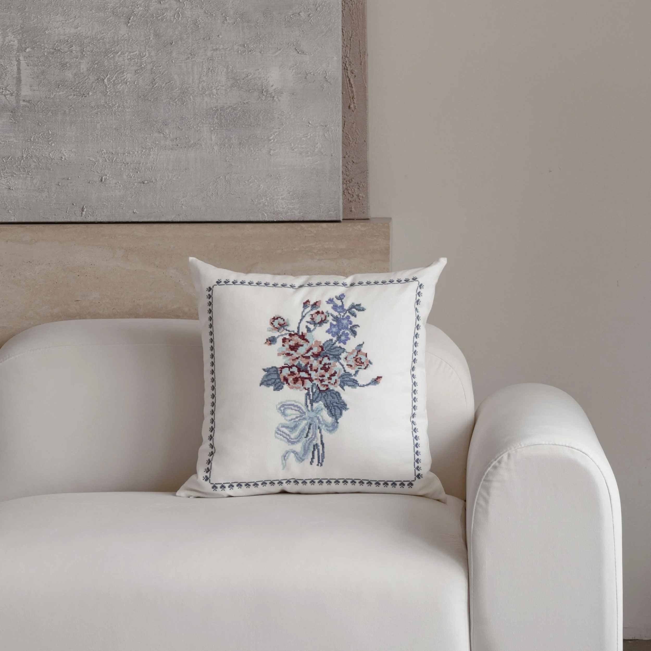Bouquet cross stitch embroidered throw pillow displayed on a white sofa in a minimalist living room
