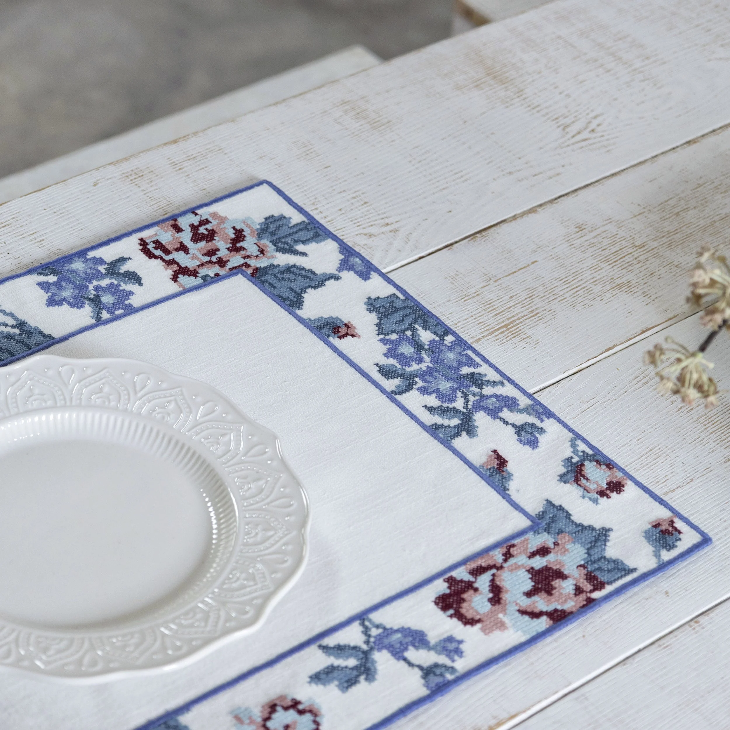 Close-up of floral cross-stitch embroidery border on a white placemat with decorative dinnerware