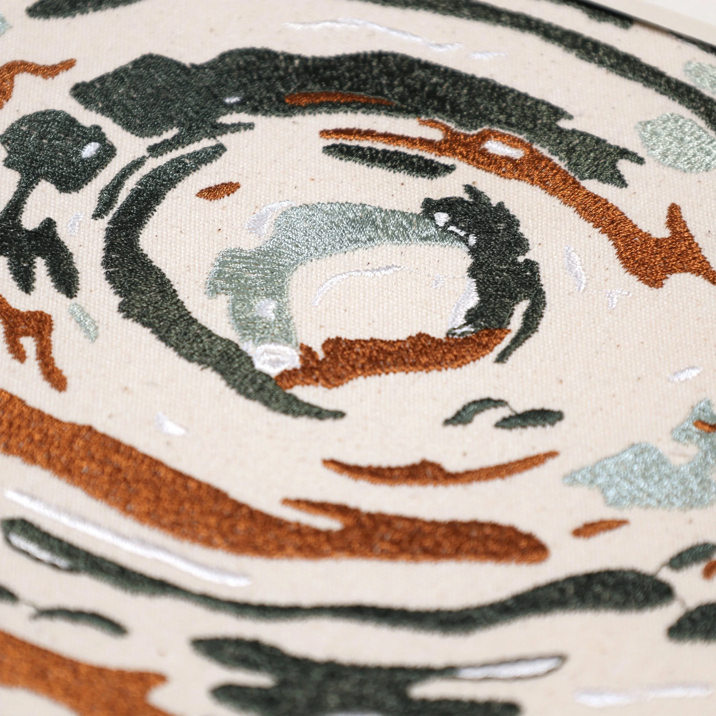 Close-up of Echoes embroidery details — green, copper, and silver thread texture forming abstract water ripples, Pam Pan embroidered wall art.