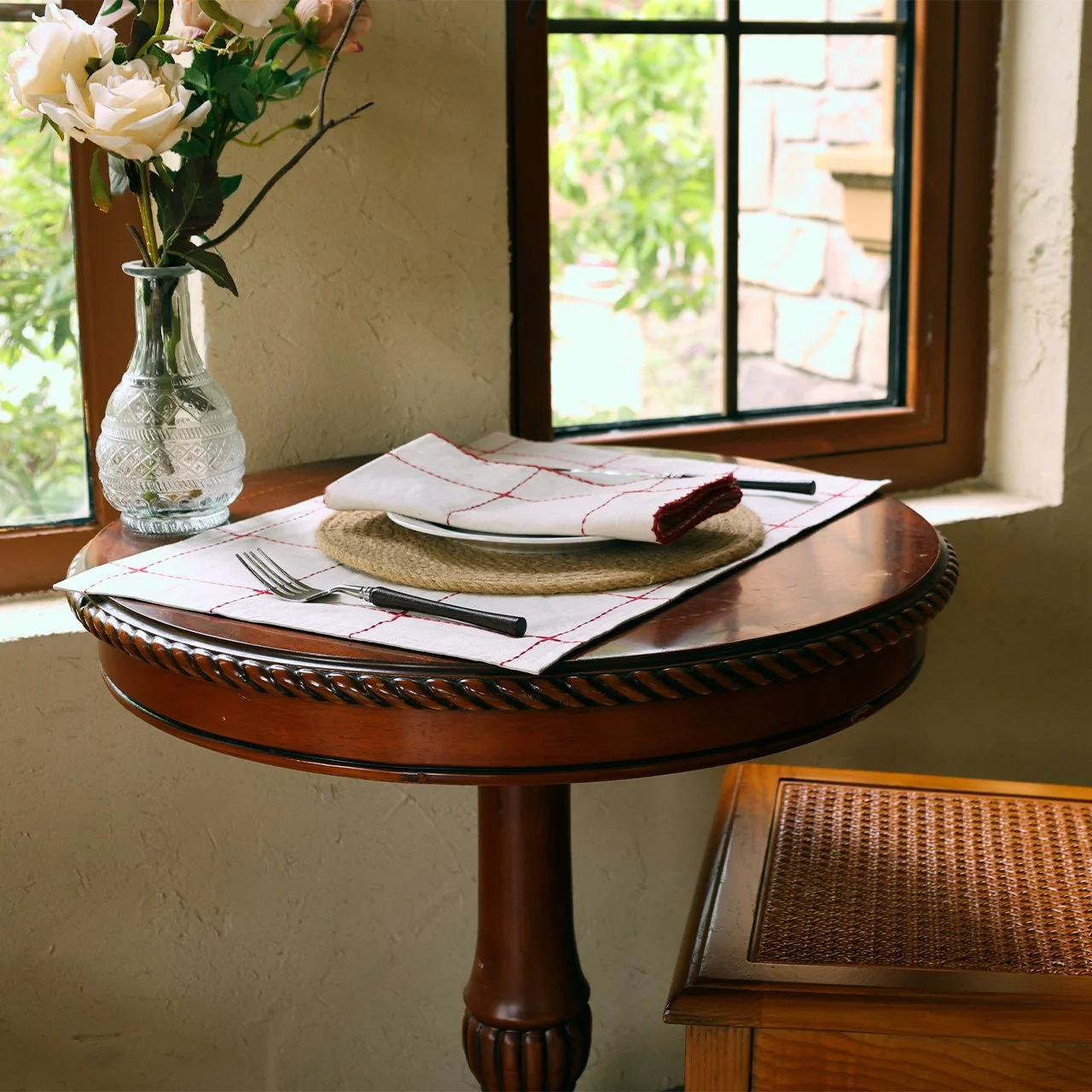 Grid embroidered placemat and napkin on a small round table beside a window