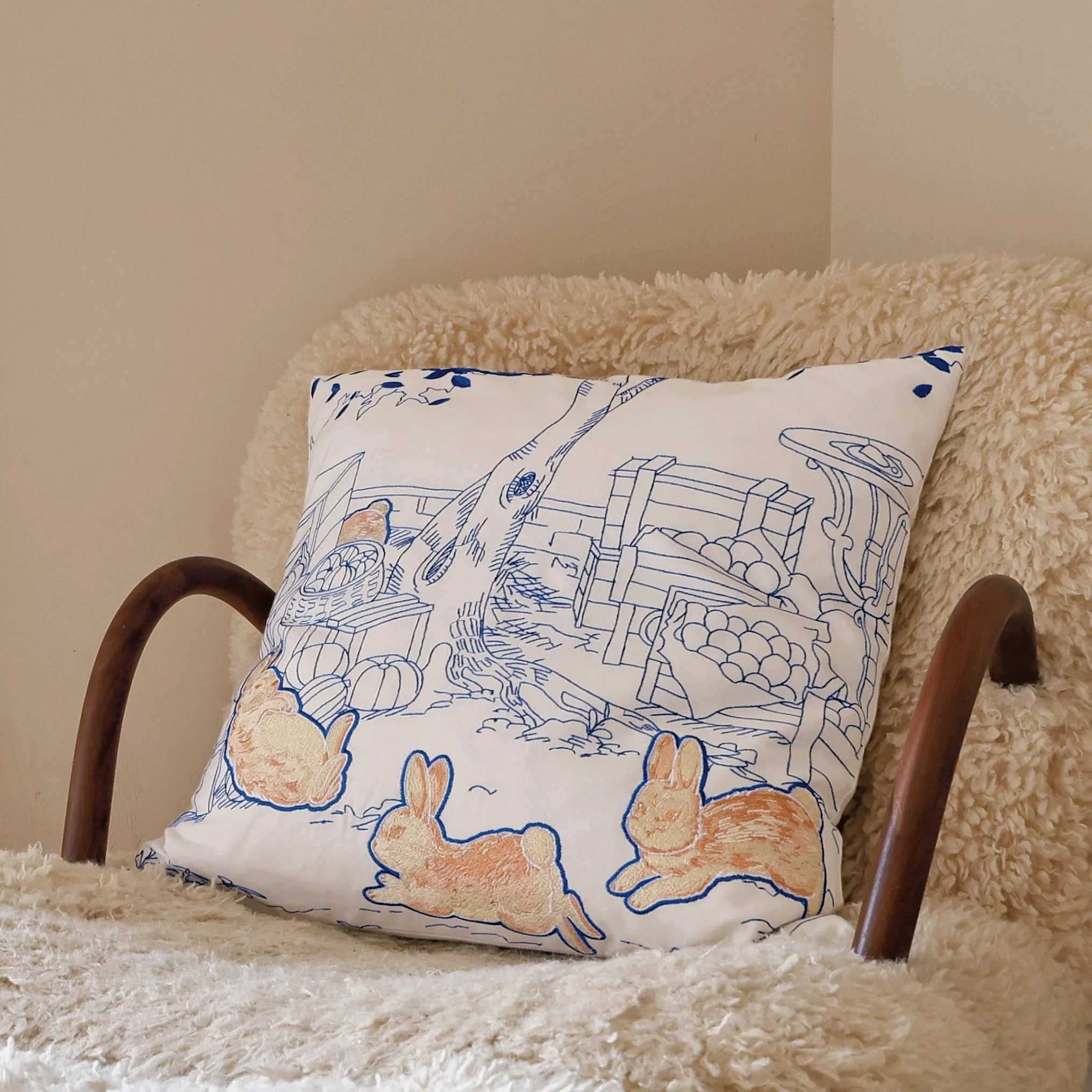 Whimsy throw pillow with delicate blue embroidery and playful brown rabbits, adding warmth to a cozy armchair.