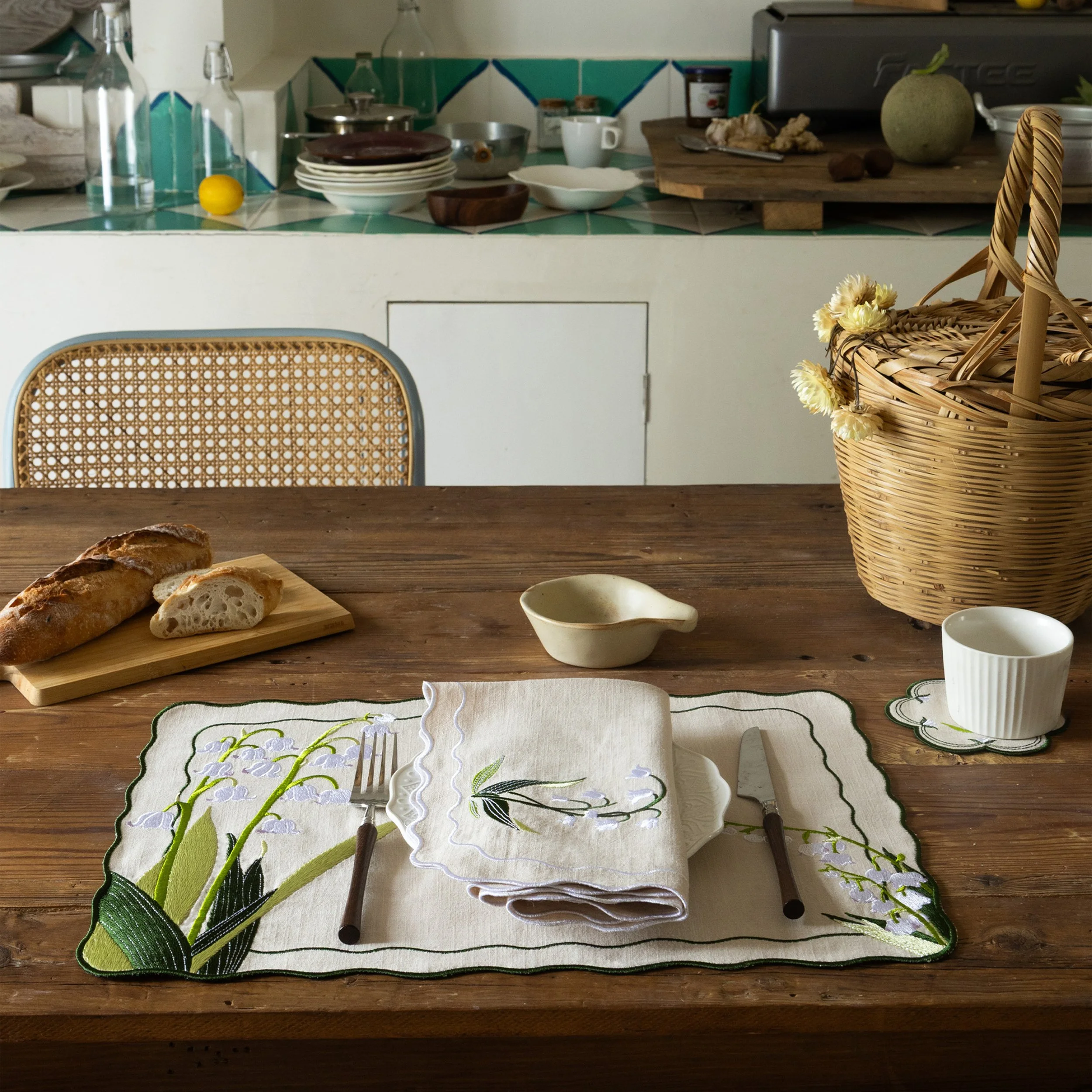 Embroidered table linen set with lily of the valley placemat, napkin, and coaster on a wooden dining table