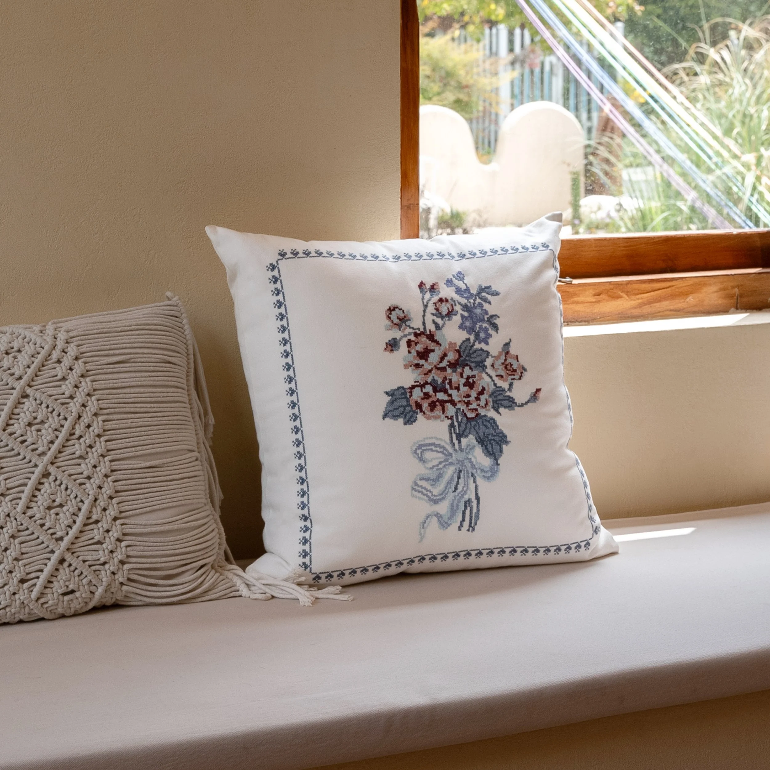 Bouquet embroidered throw pillow with vintage-inspired floral cross stitch design resting on a sunlit window seat