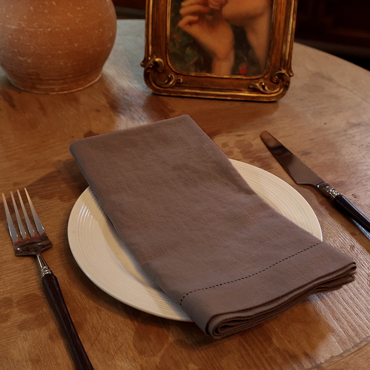 Dark brown hemstitched ramie cotton napkin folded on a white plate