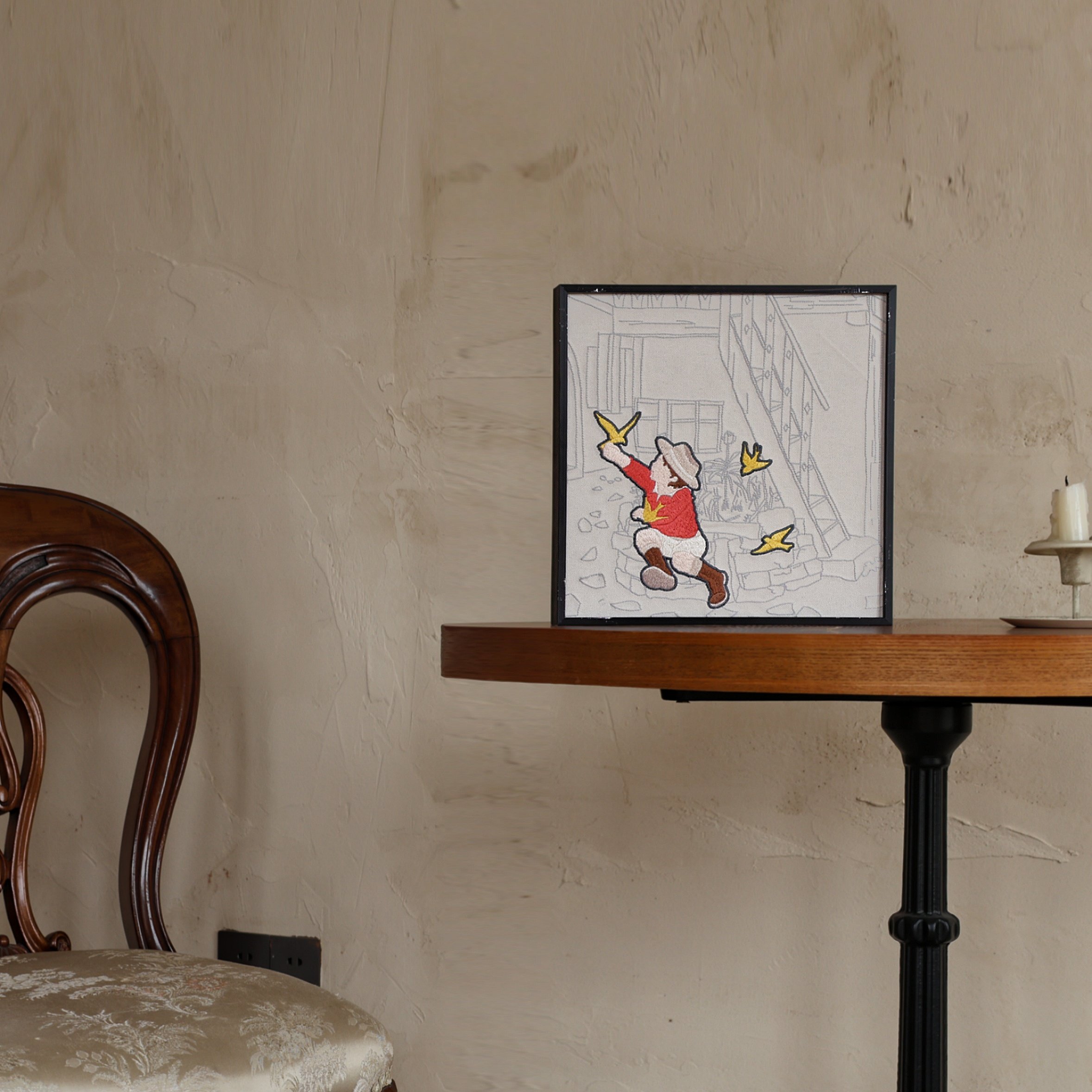 Embroidery wall art piece of child chasing bird from the Wild Corner set on a around table
