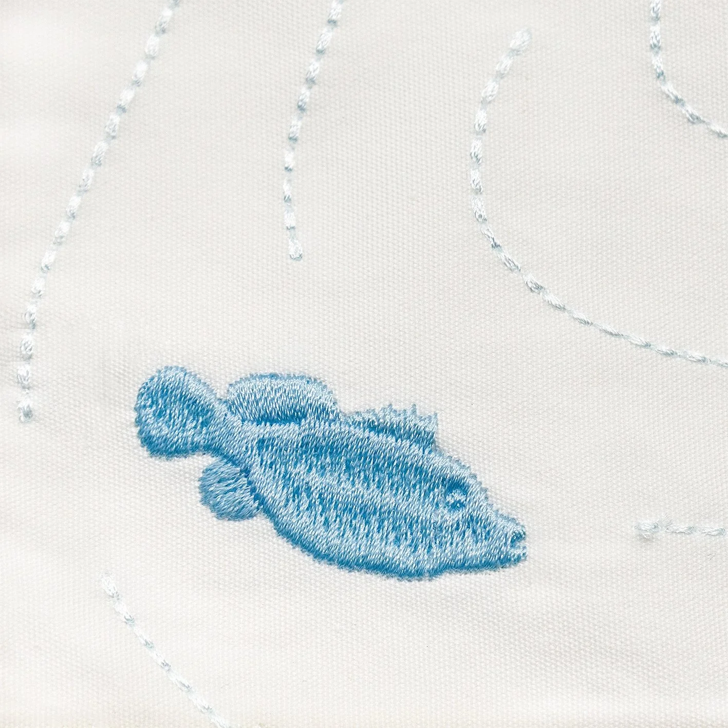 Fine embroidery details of the blue fish motif on the Aqua Series placemat. Tonal threads depict fluid underwater movement.