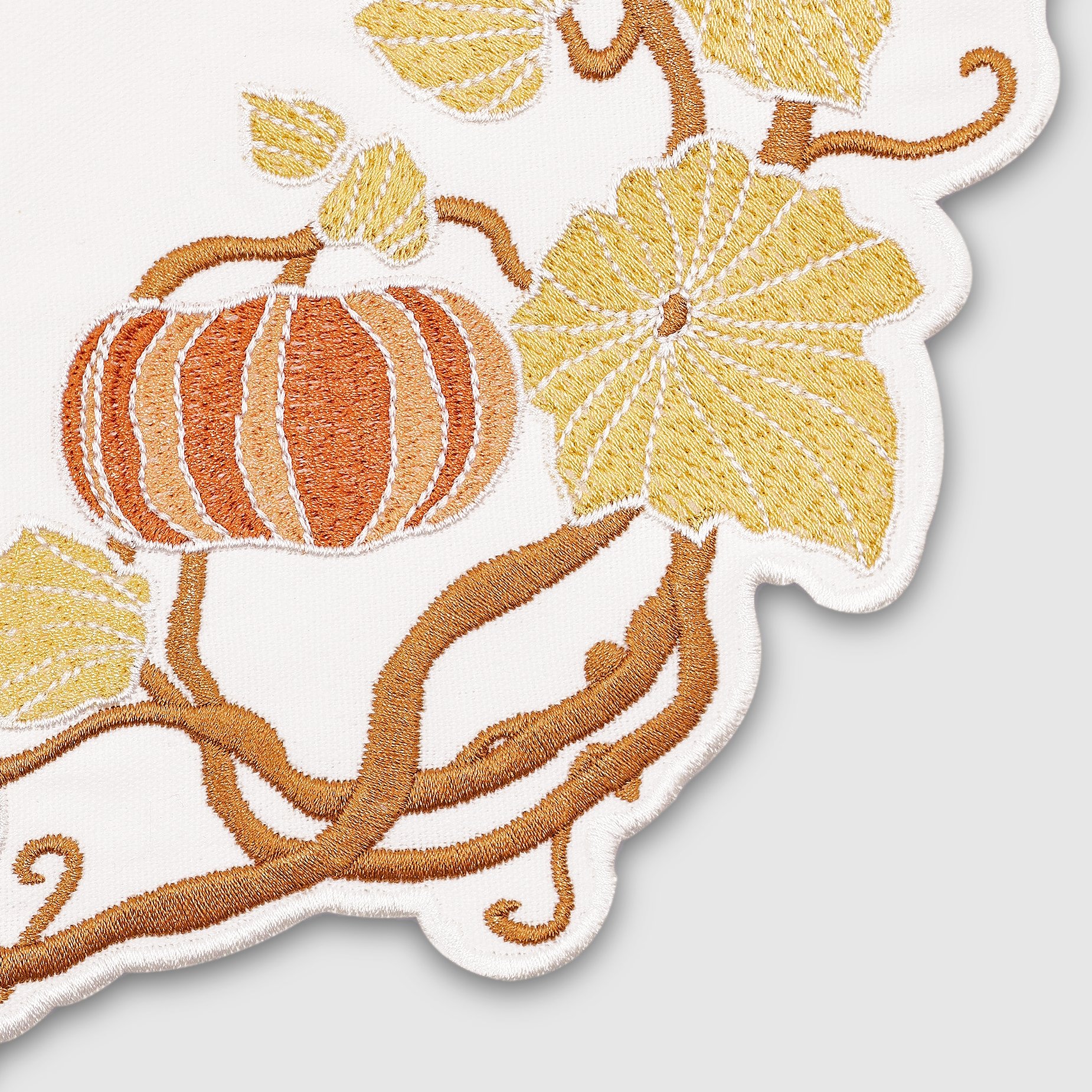 Close-up embroidery detail of pumpkin and leaf on cotton placemat — fine stitching craftsmanship from Pam Pan Pumpkin Series.