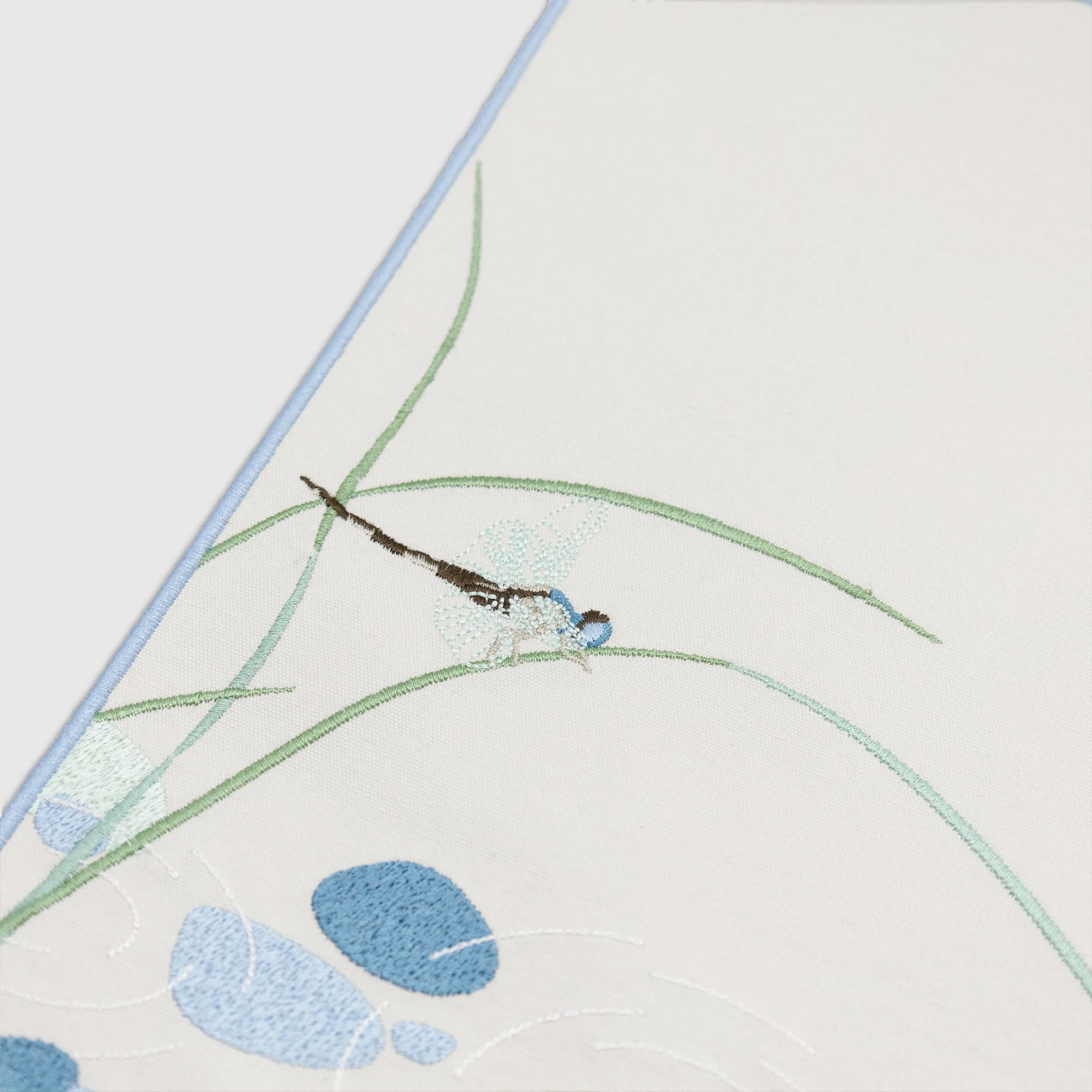 Close-up detail of dragonfly embroidery and reed motifs on the Riparia embroidered placemat