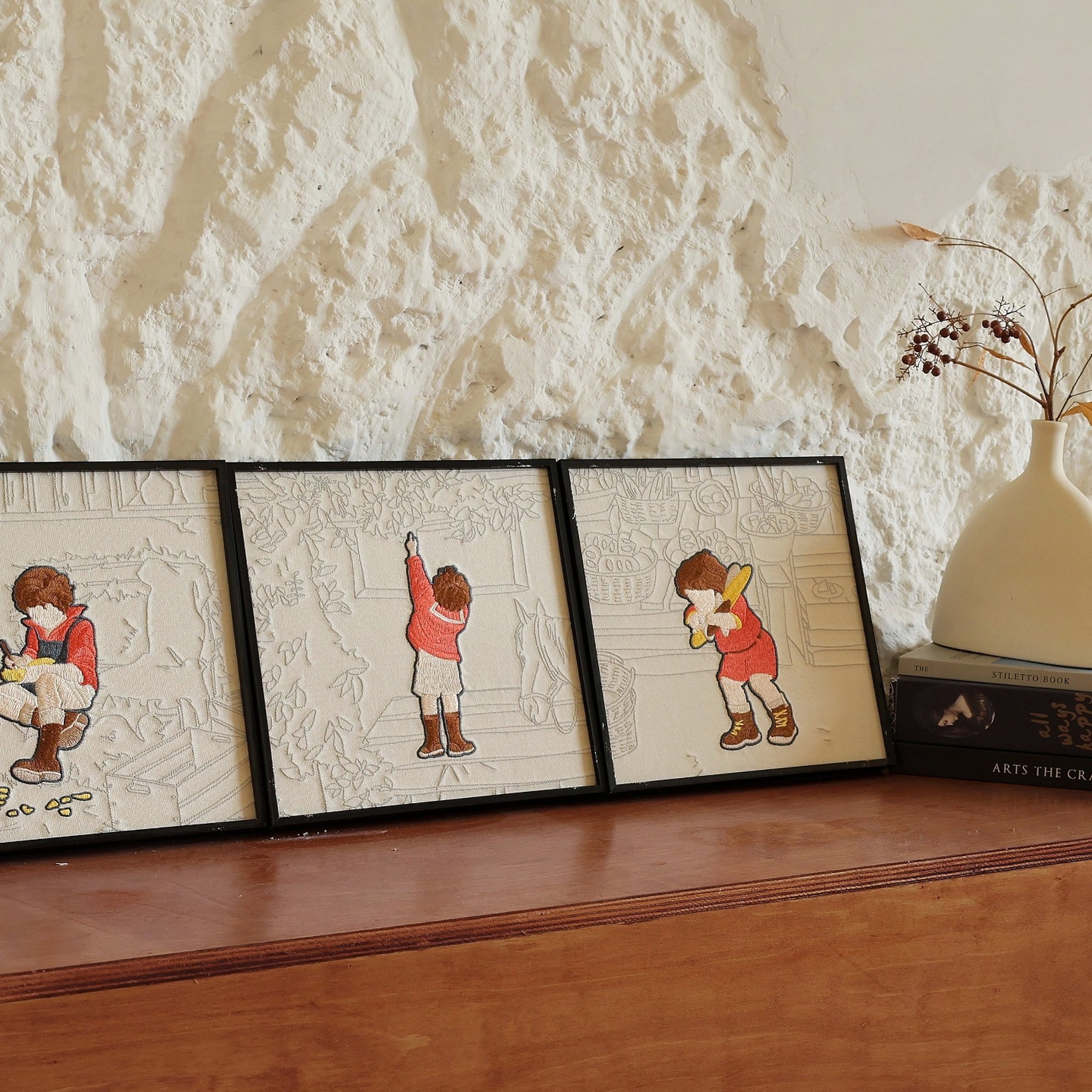 Square embroidered framed art of childhood little things placed on a counter against textured white wall