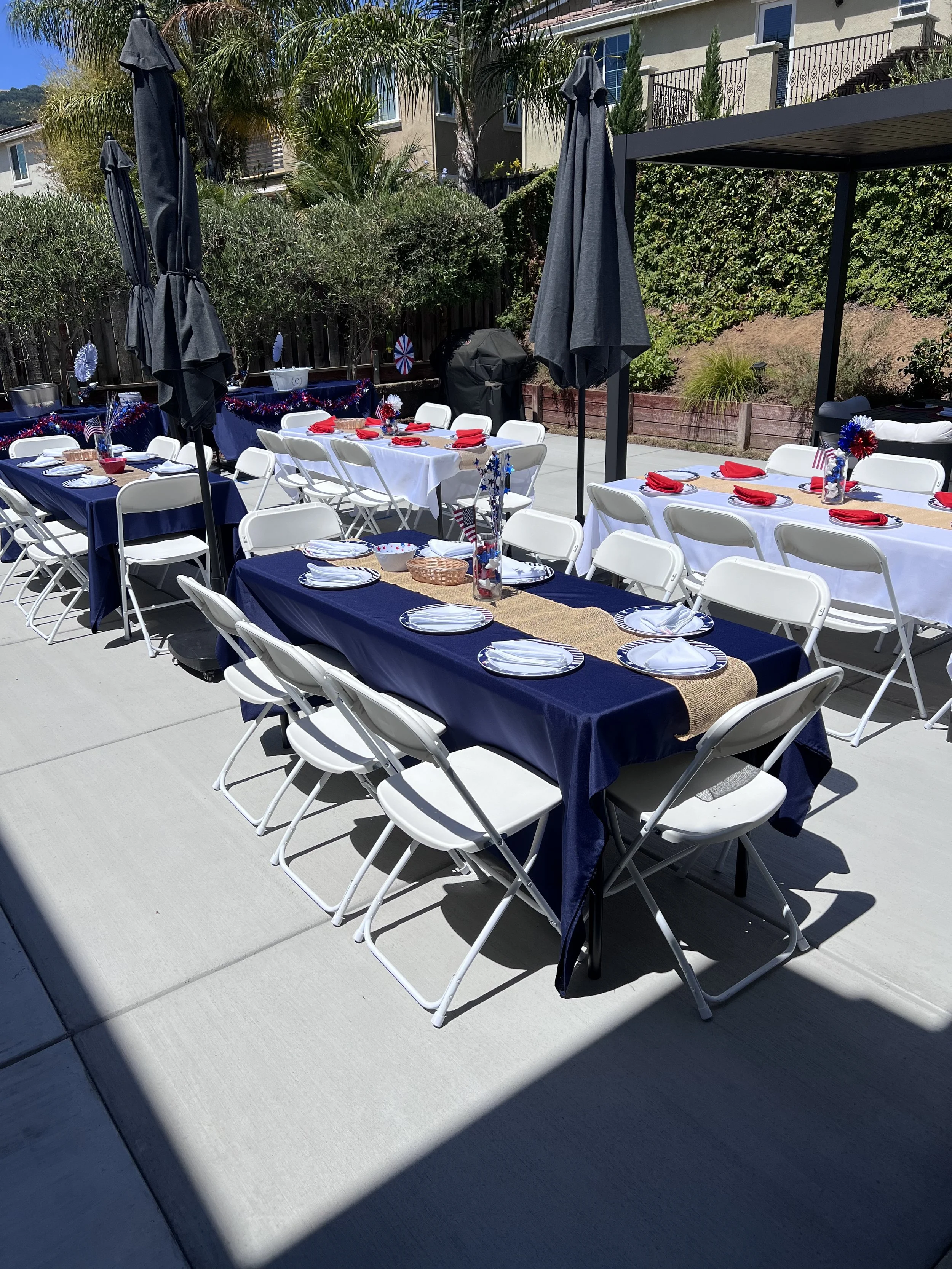 White folding chairs and tables with navy linens set up for a Fourth of July backyard party