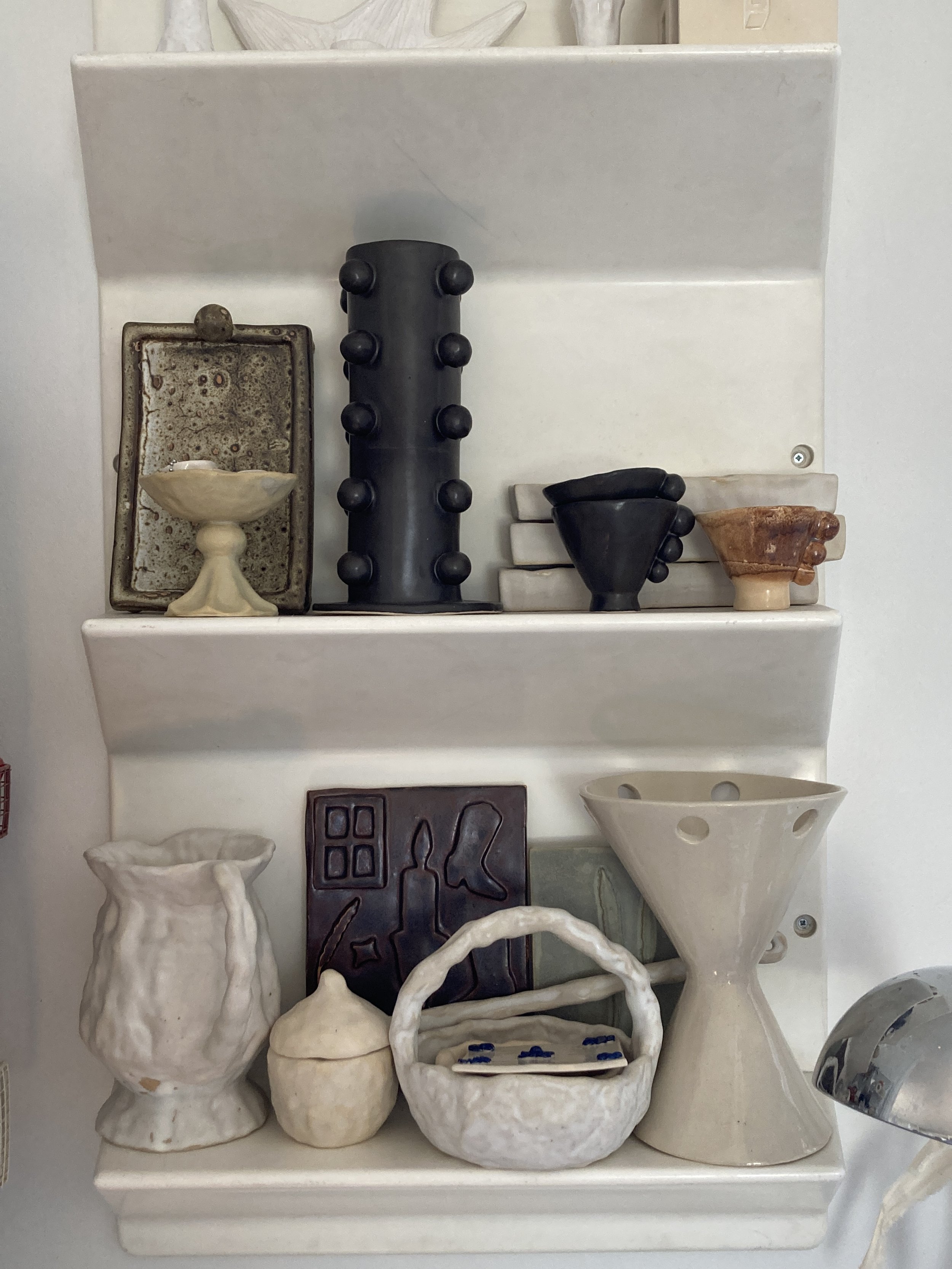 Collection de céramiques blanches, comprenant vases, plat, et sculptures, posés sur une étagère.