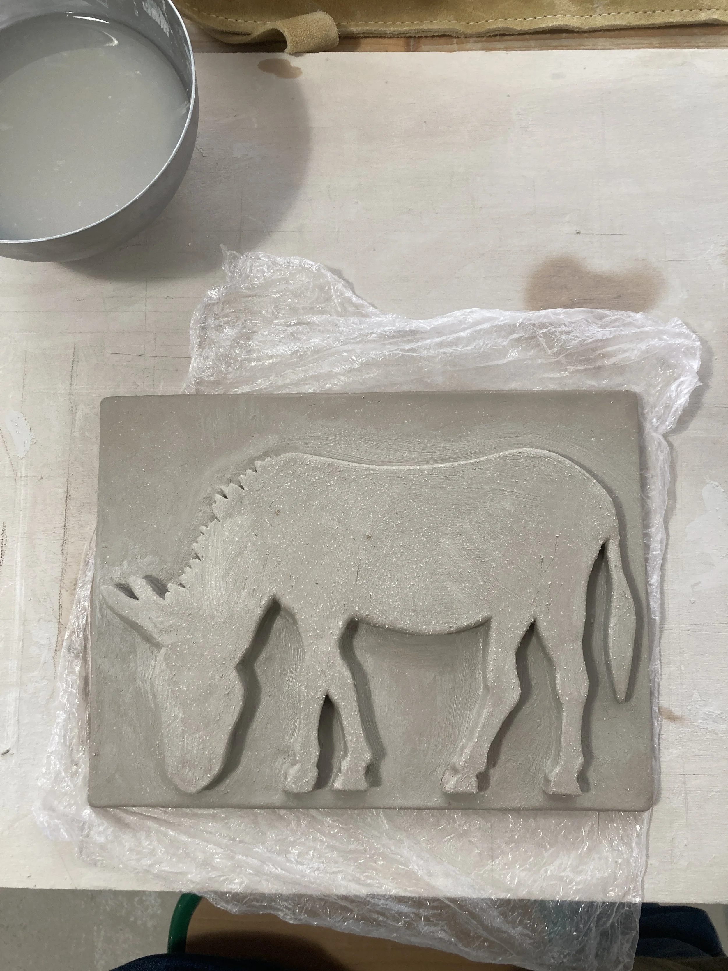 Un bas-relief en argile avec la forme d'un âne, posé sur une surface en bois d'atelier.