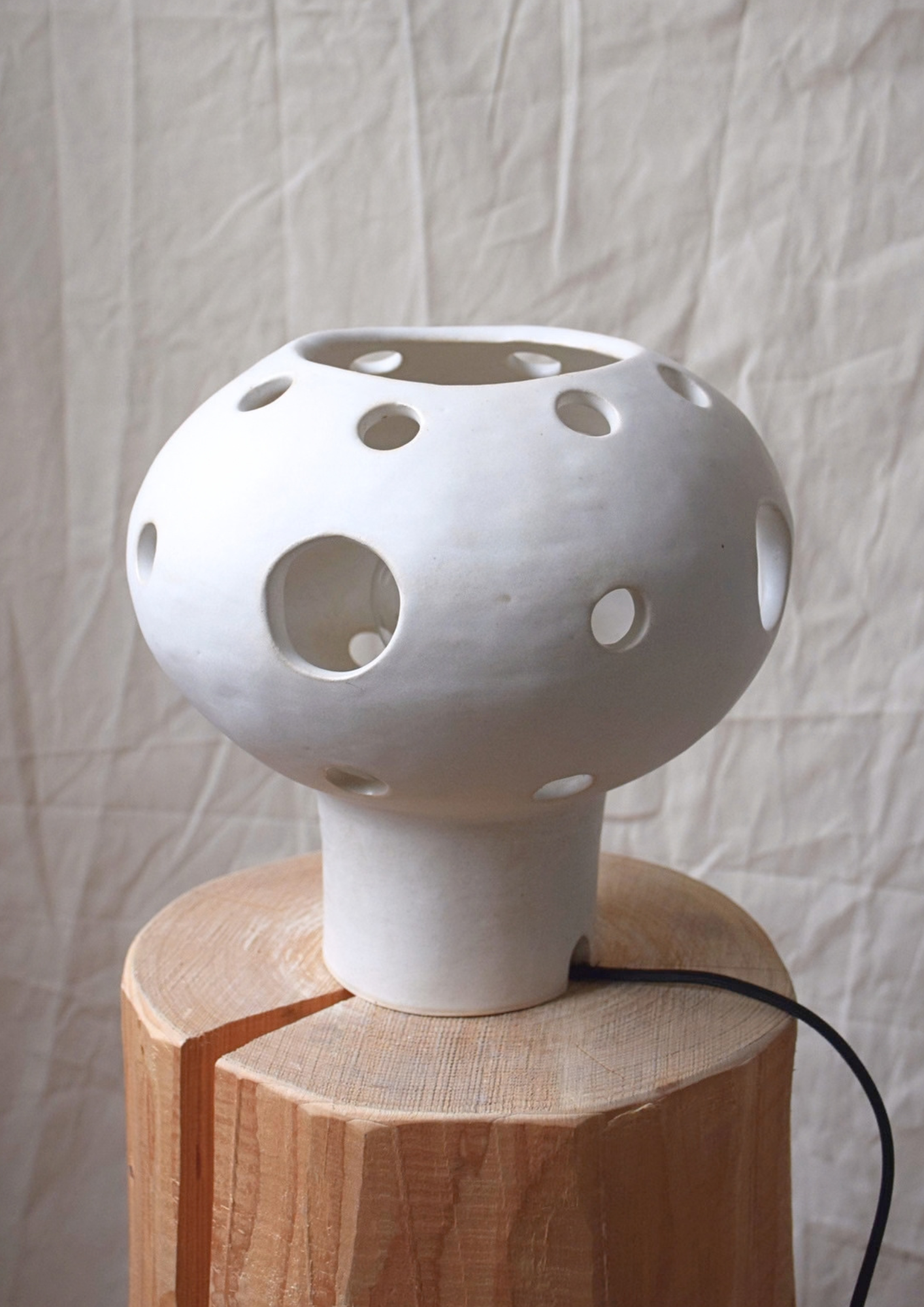 Lampe en céramique blanche avec des trous ronds, posée sur un support en bois.»