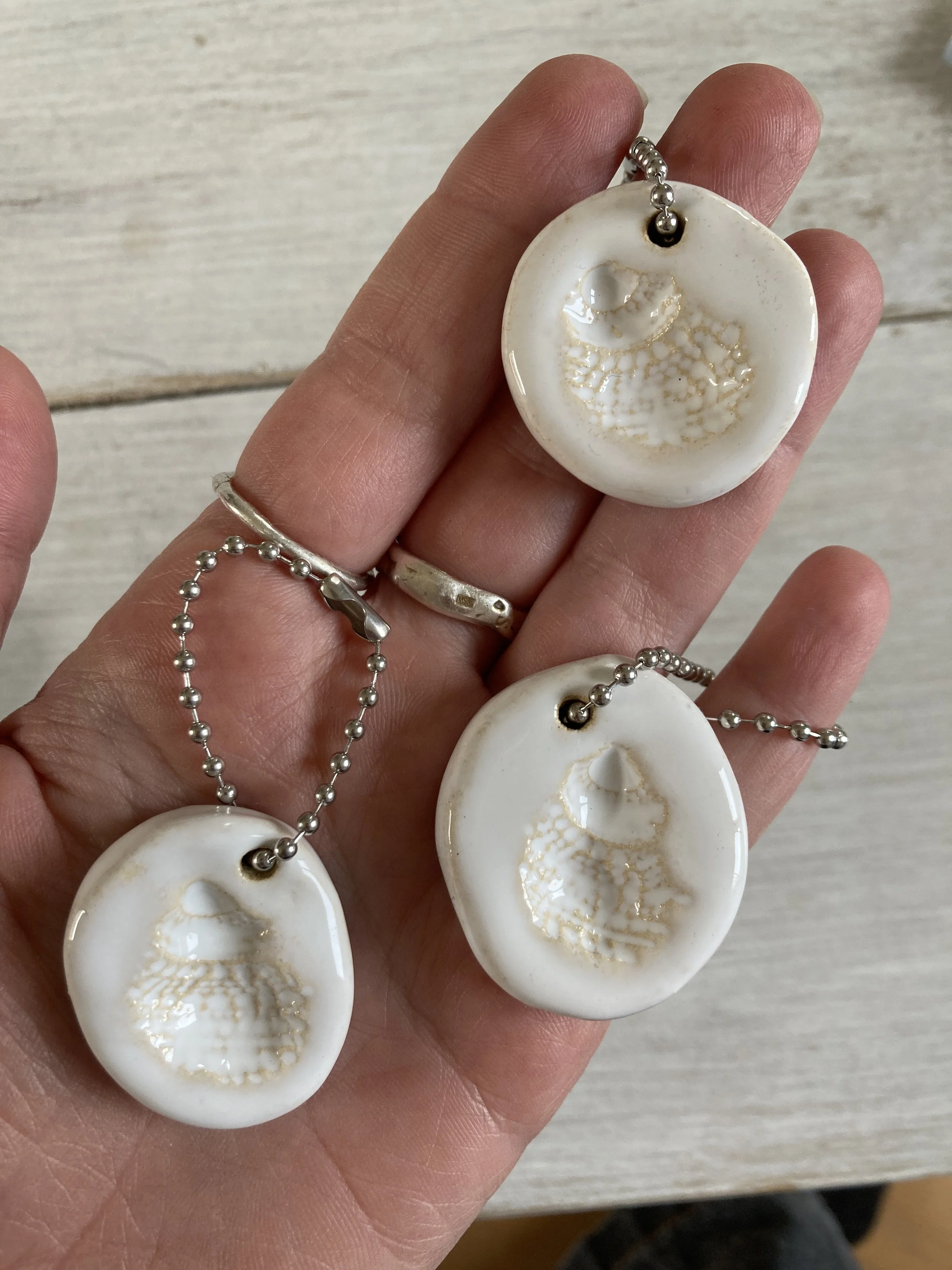 L'image montre des pendentifs en forme de coquillage tenus dans une main.