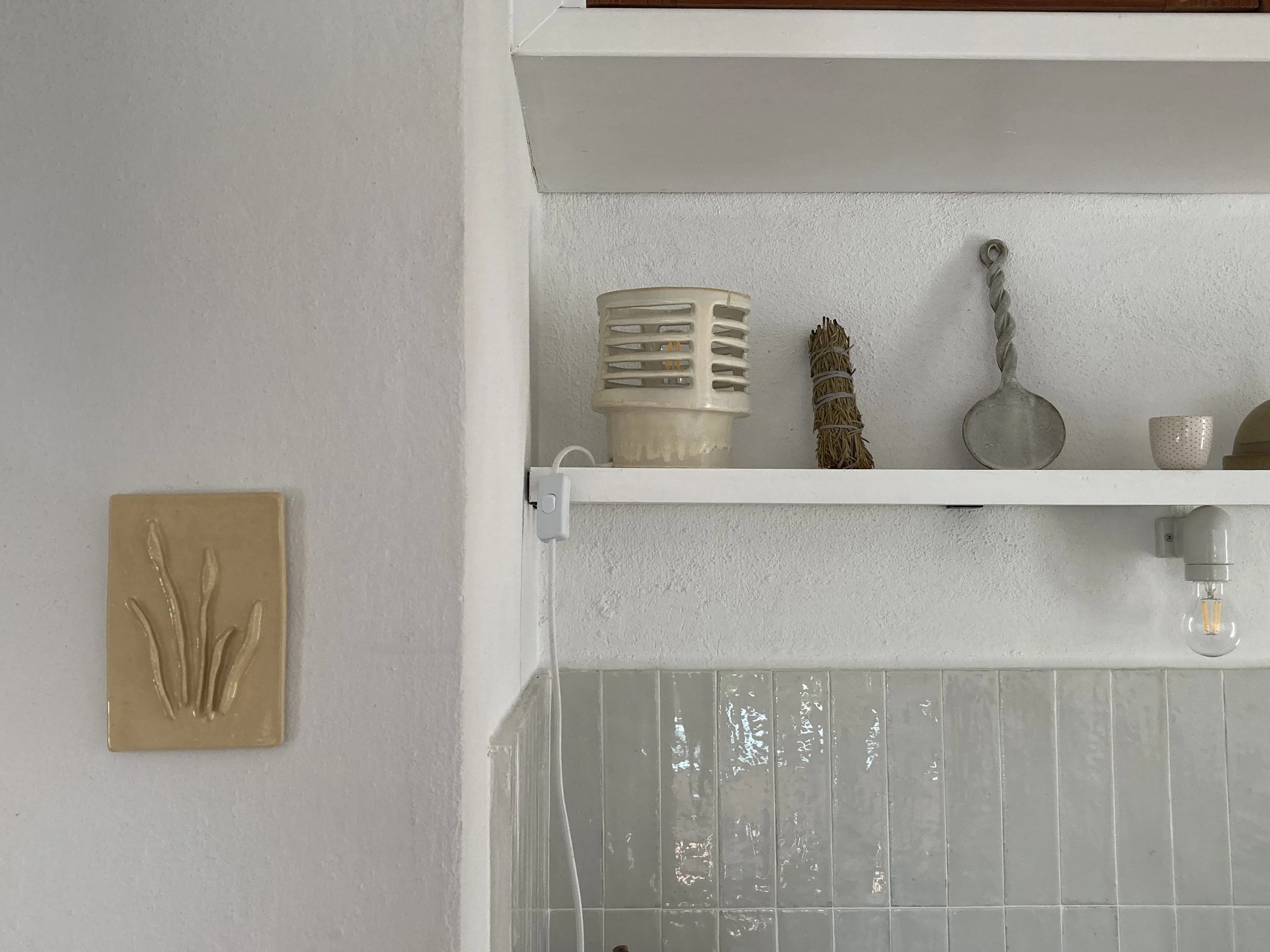 Mur blanc avec sculpture abstraite en bas-relief, lampe en céramique dans le fond sur étagère.