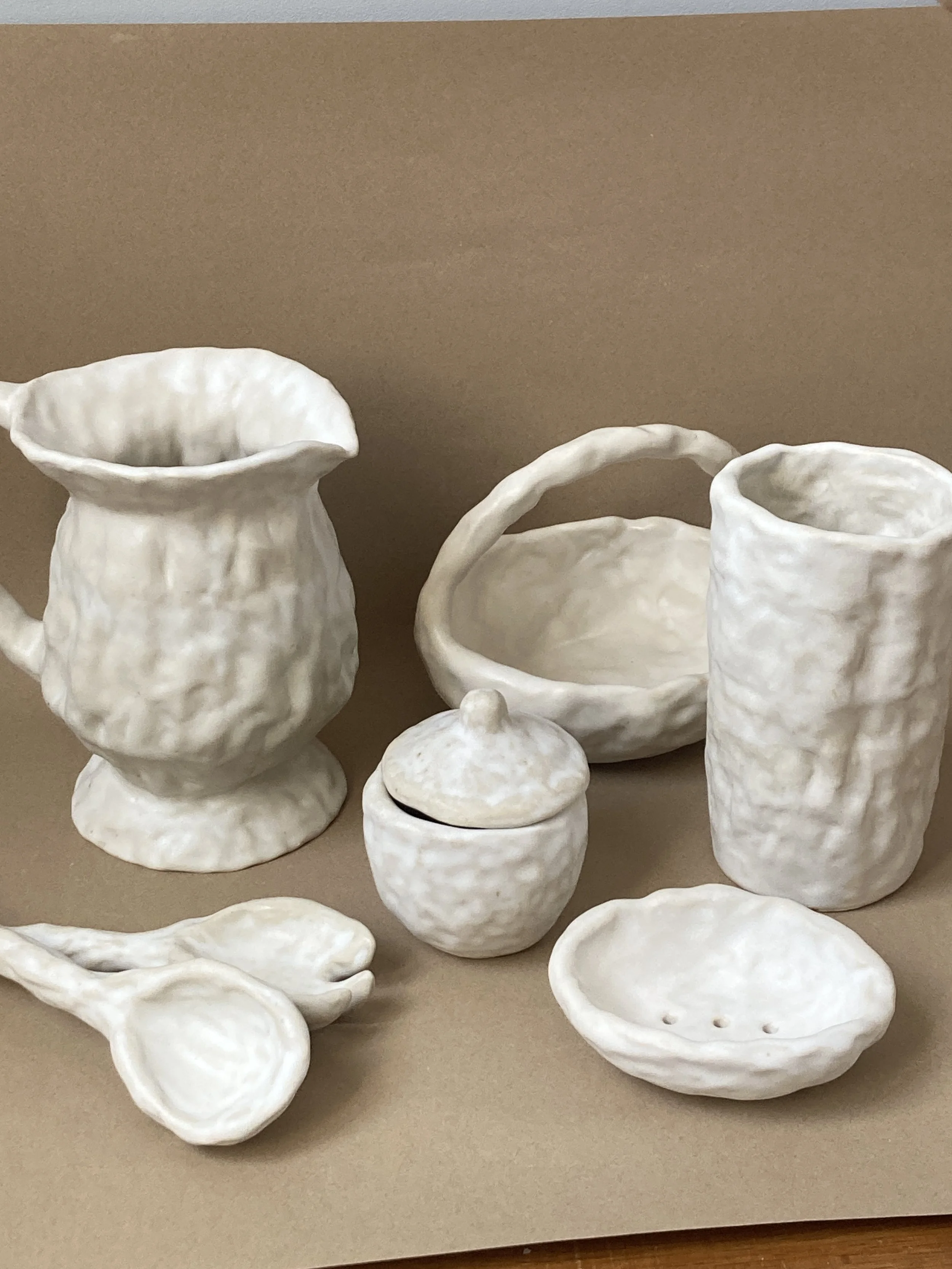 Une collection de vaisselle en céramique blanche, comprenant des vases, des bols, des plats, et un couvercle, exposés sur un fond beige.